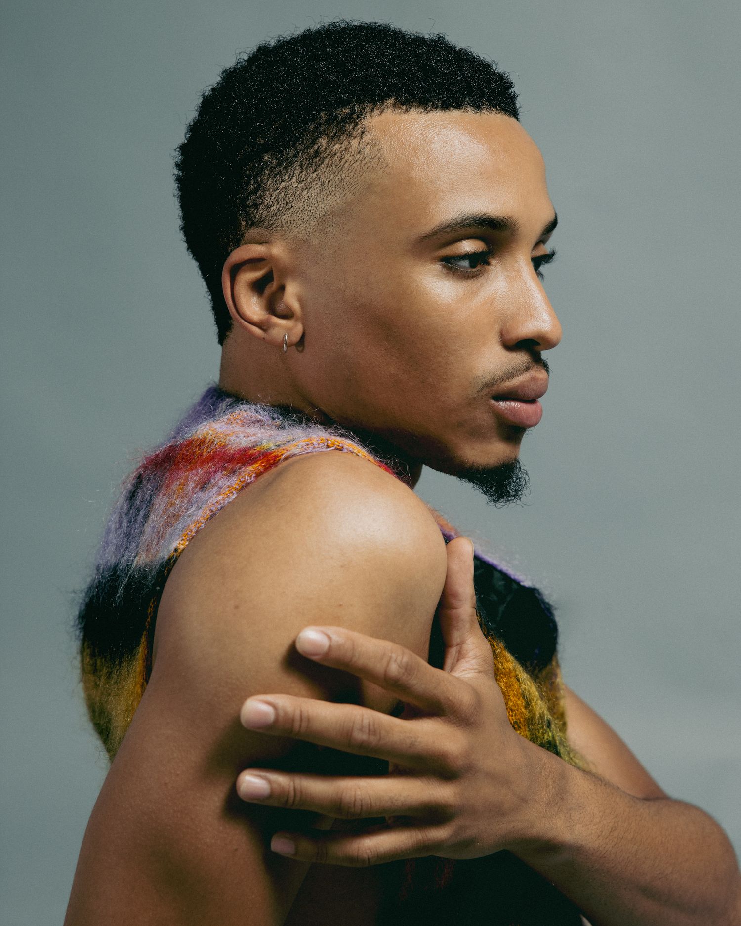 Artistic portrait of person in profile view wearing colorful paint on bare shoulders against gray background.