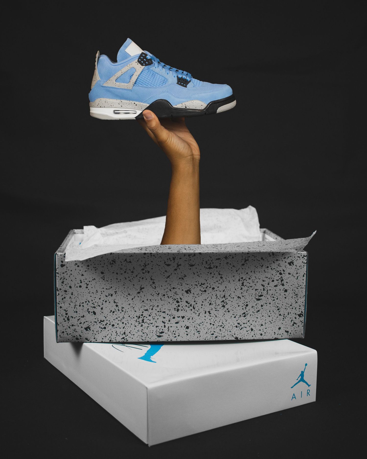 A sequence showing a light blue Air Jordan sneaker emerging from a concrete block on a white box background.