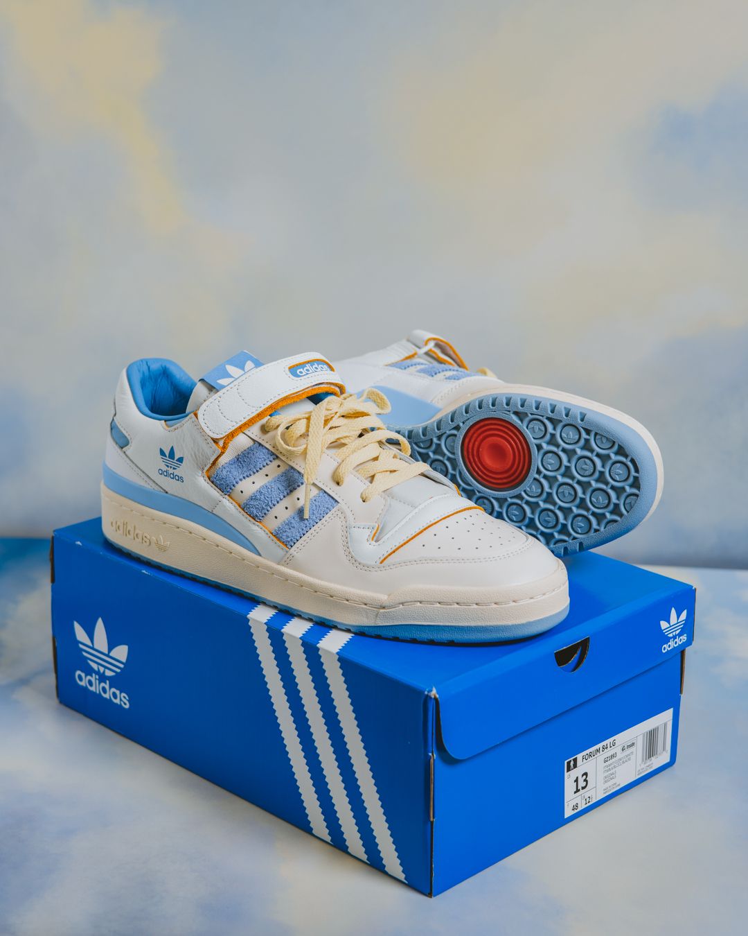 White and blue Adidas Forum low sneakers displayed at various angles with original blue box packaging.