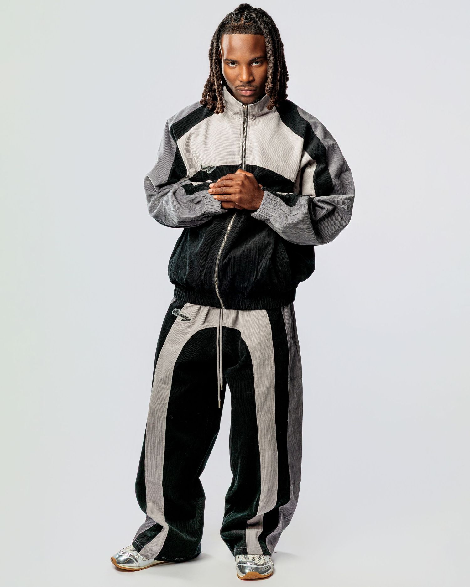 Athletic figure wearing a black and gray color-blocked tracksuit with coordinating jacket and pants against white background.