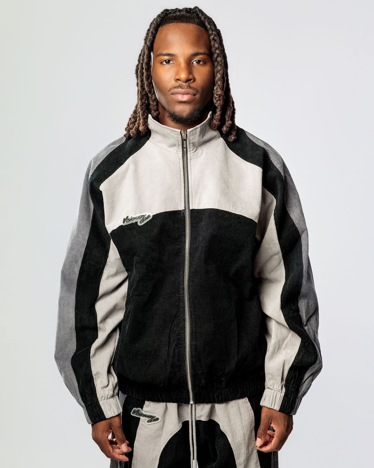 Athletic colorblock jacket in black, white and grey with zip front closure and hood worn by a model against light background.