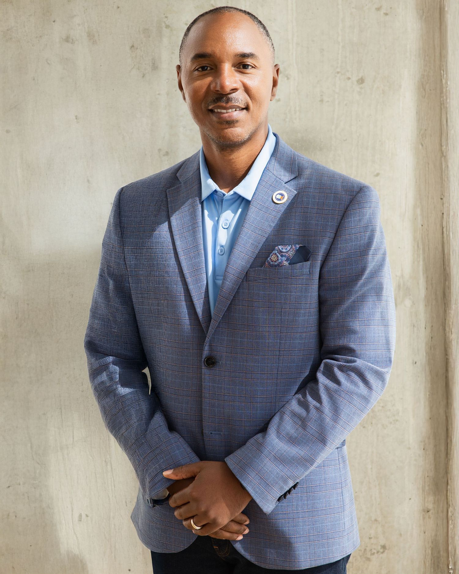 Professional wearing a blue-gray suit and light blue dress shirt poses confidently against a concrete wall.