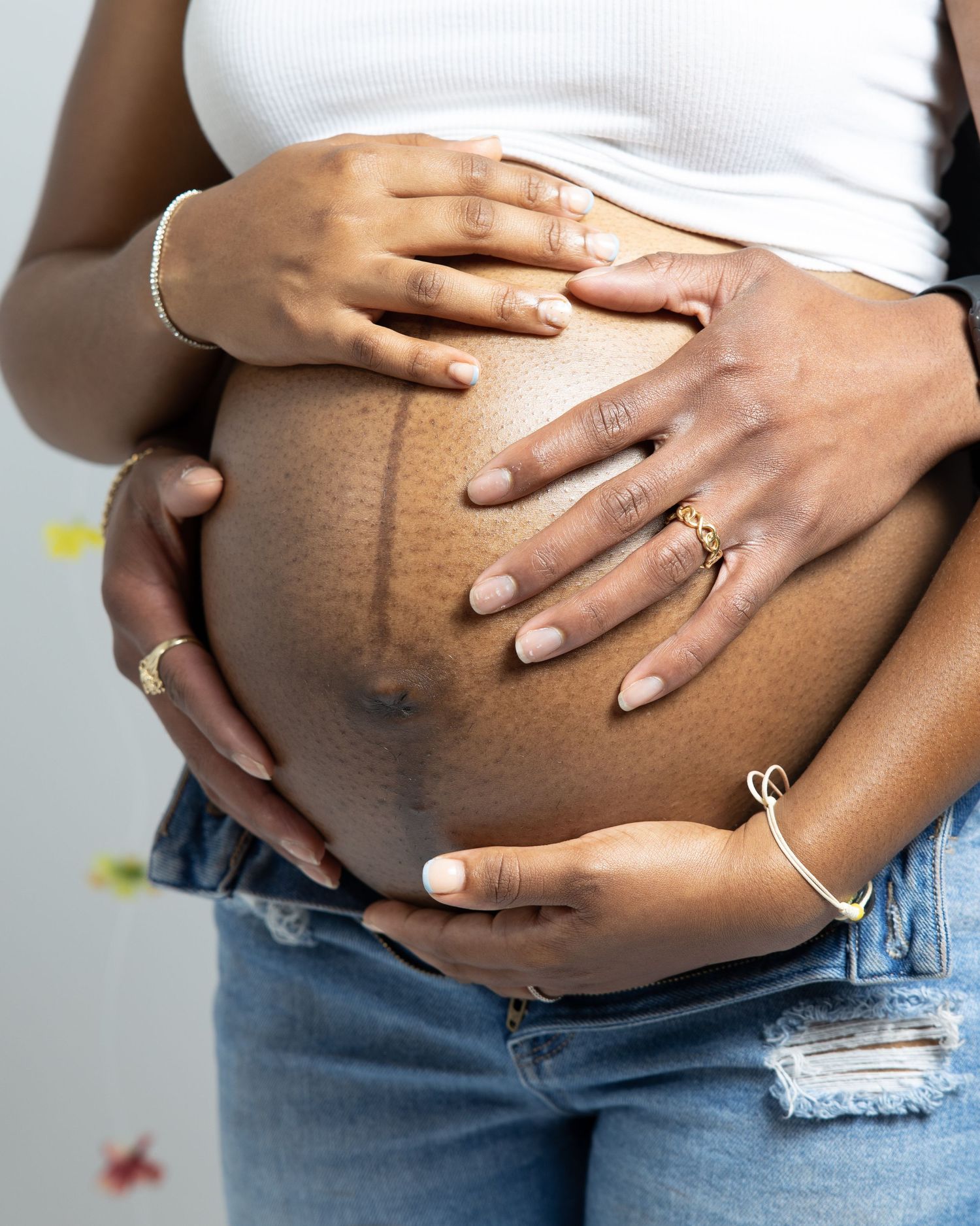 Pregnant woman in ripped jeans and white top cradles her bare belly showing linea nigra stretch mark.