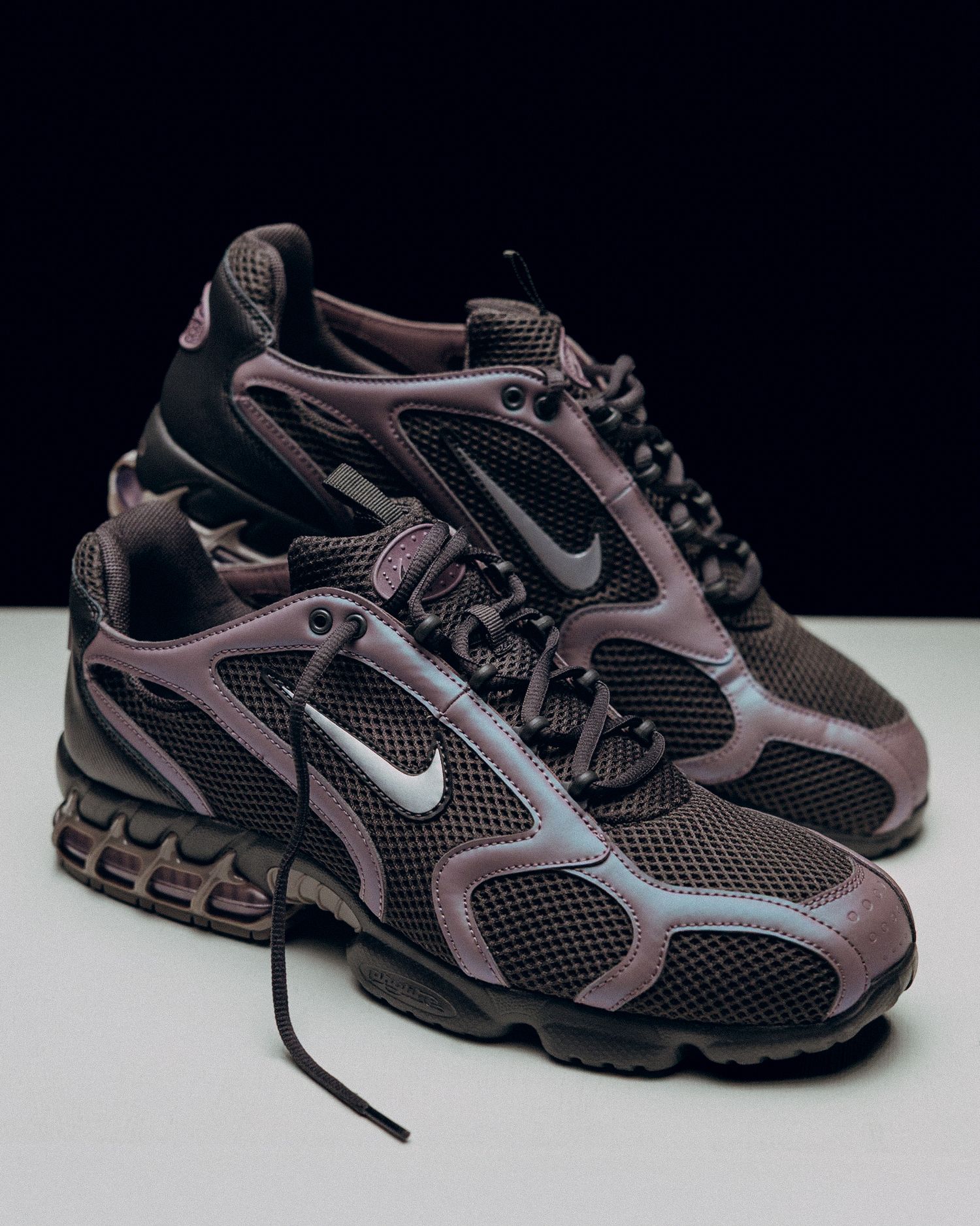 Nike athletic sneakers in black and metallic brown with mesh panels and chunky rubber soles photographed on white surface.