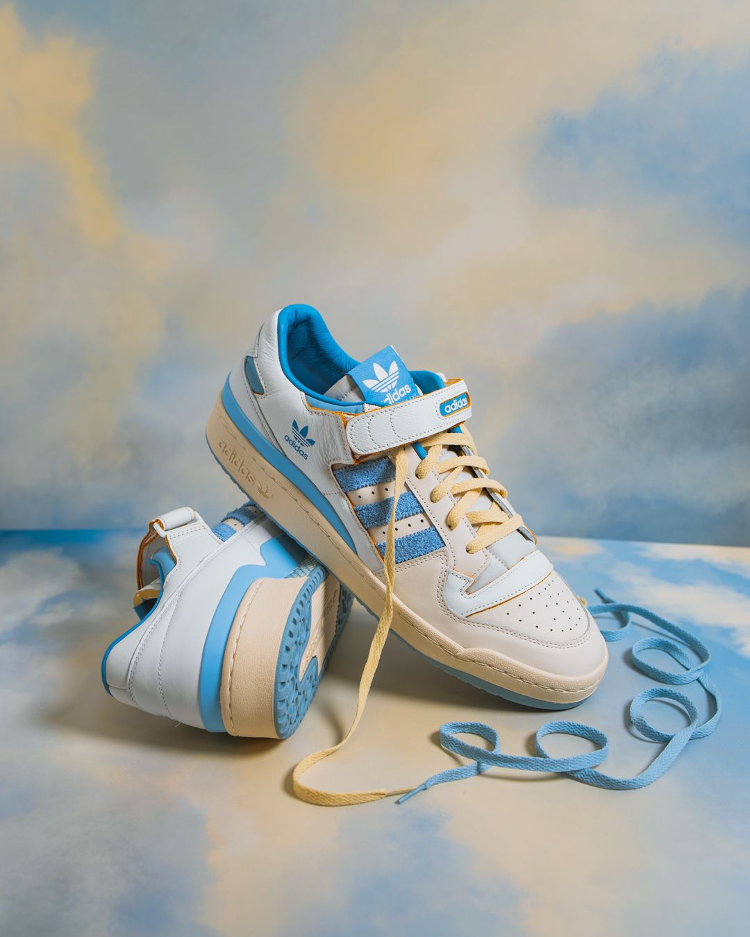 White and light blue baby sneakers arranged in a creative composition against a cloudy sky background.
