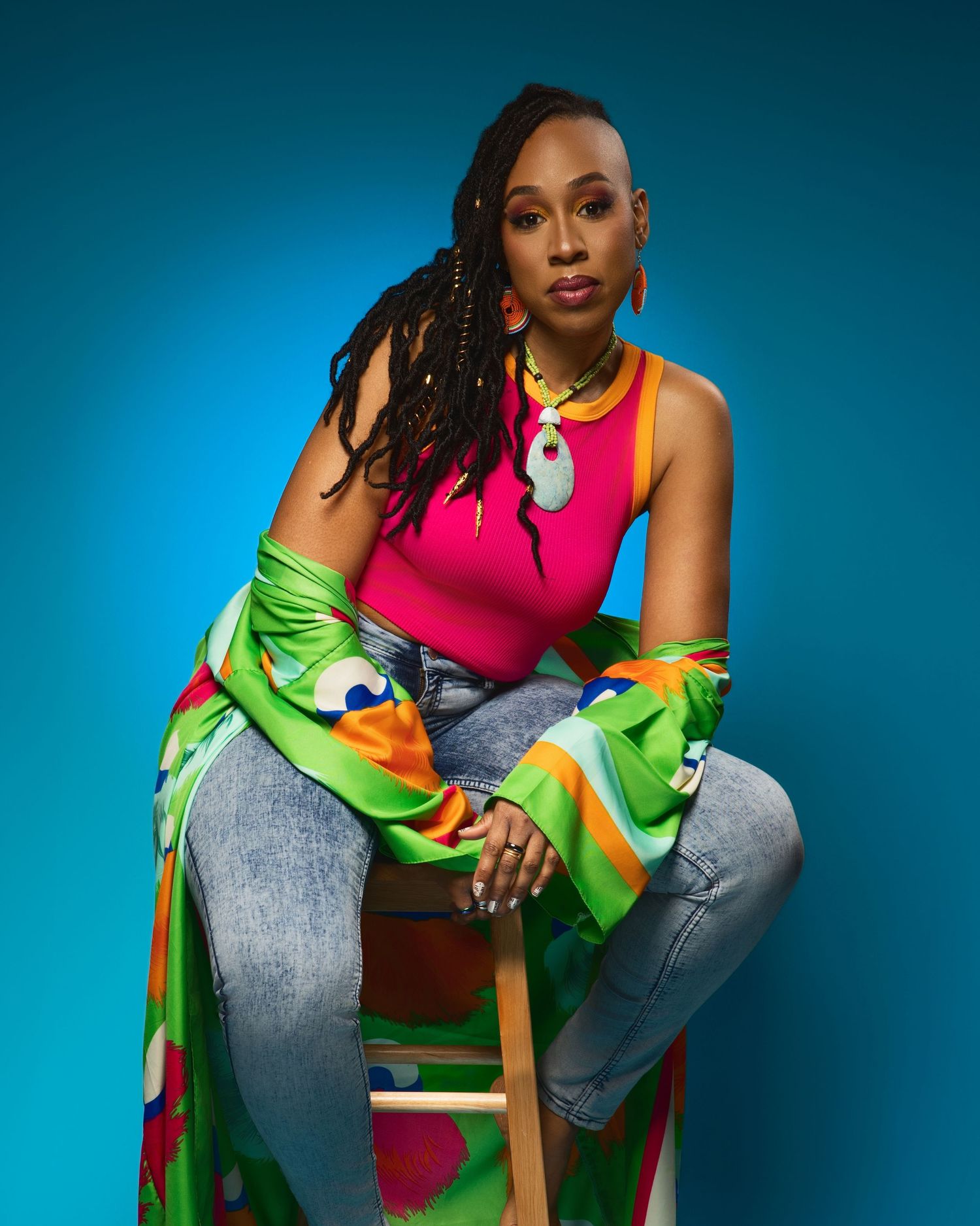 Portrait in casual wear with bright pink tank top and colorful kimono against blue background.