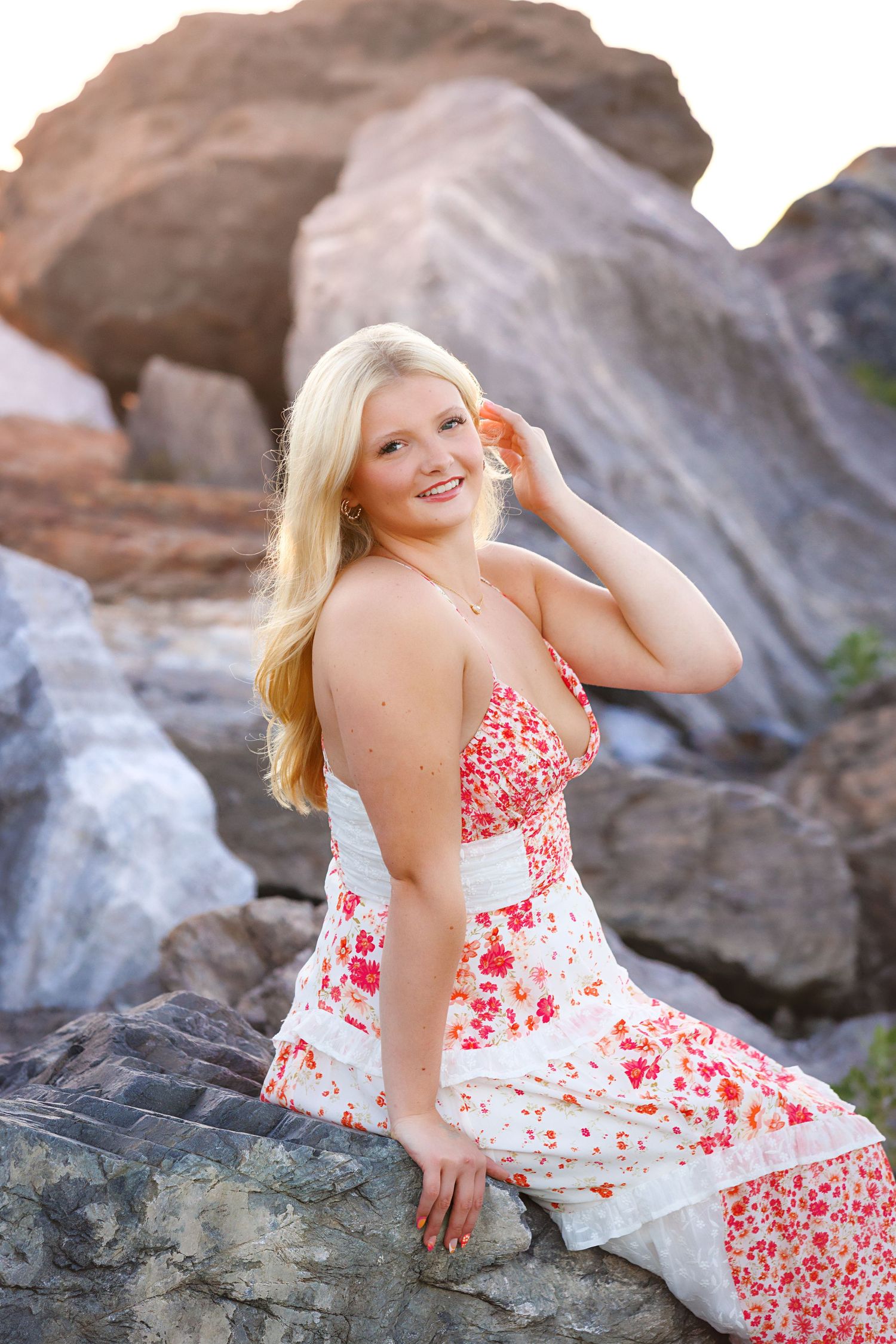A person in a red and white floral dress poses on rocky terrain during an outdoor photo session.