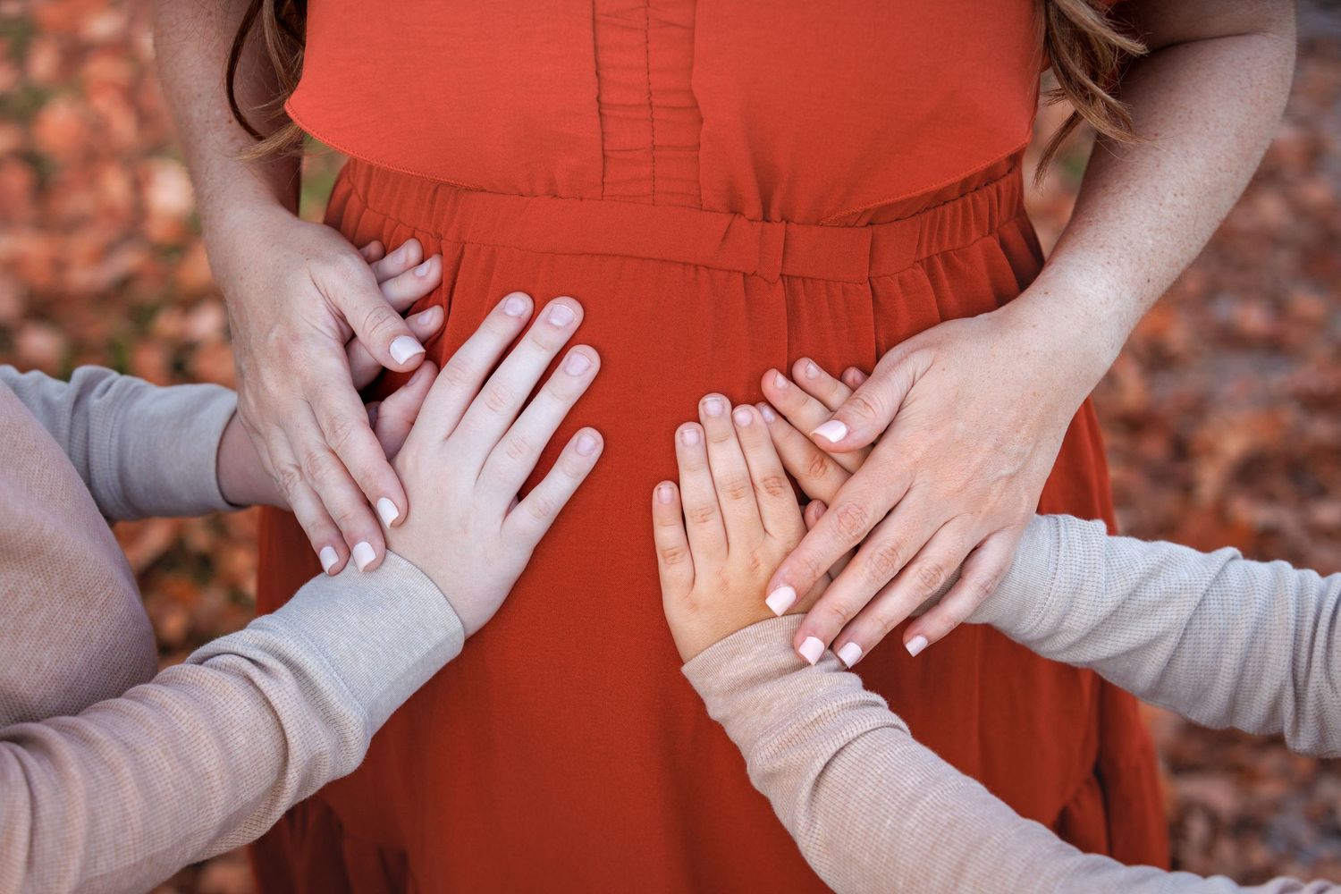 Small hands reach out to touch a person wearing a red dress against an autumn background with fallen leaves.