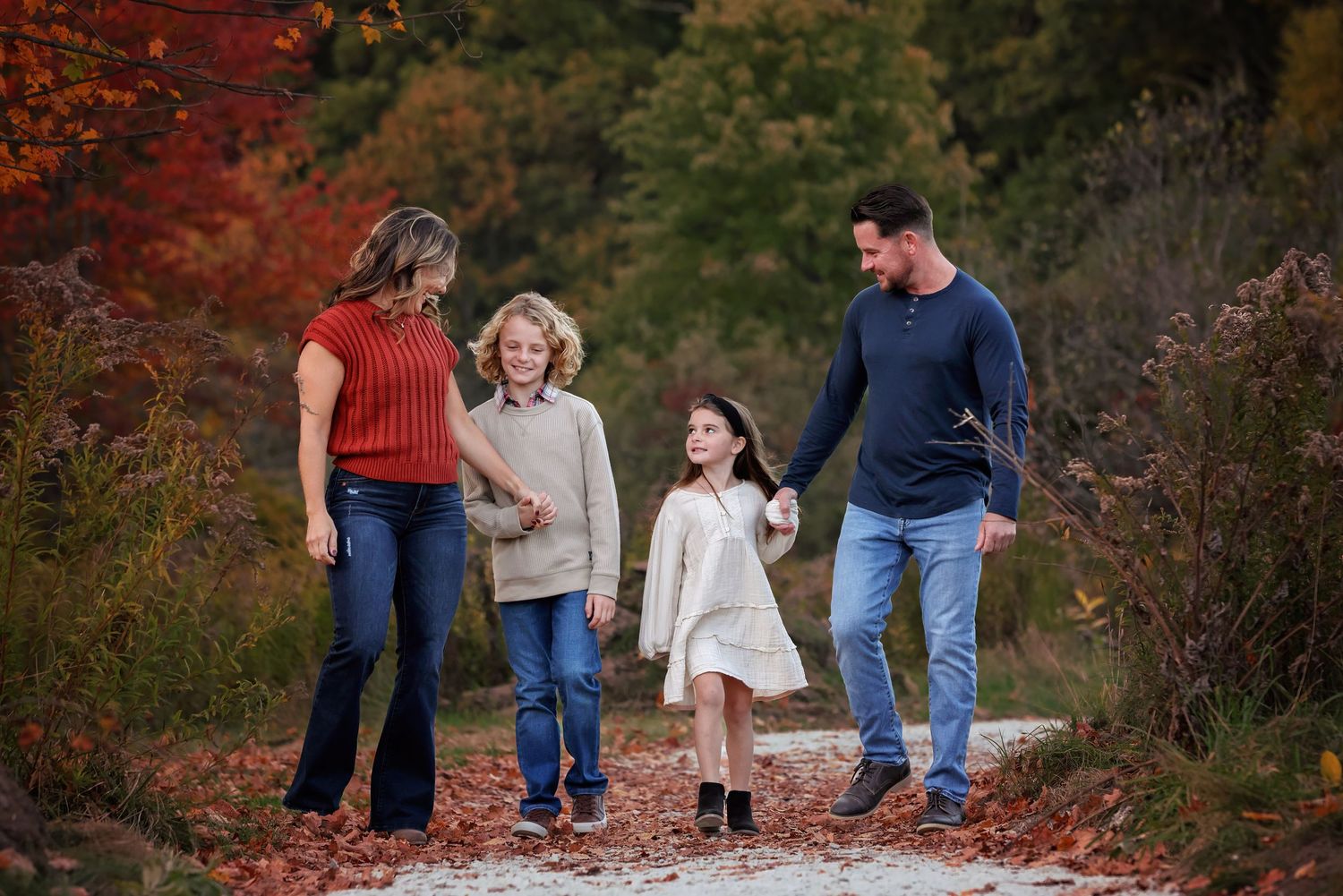 A family walks together on a winding path surrounded by vibrant red autumn foliage and trees.