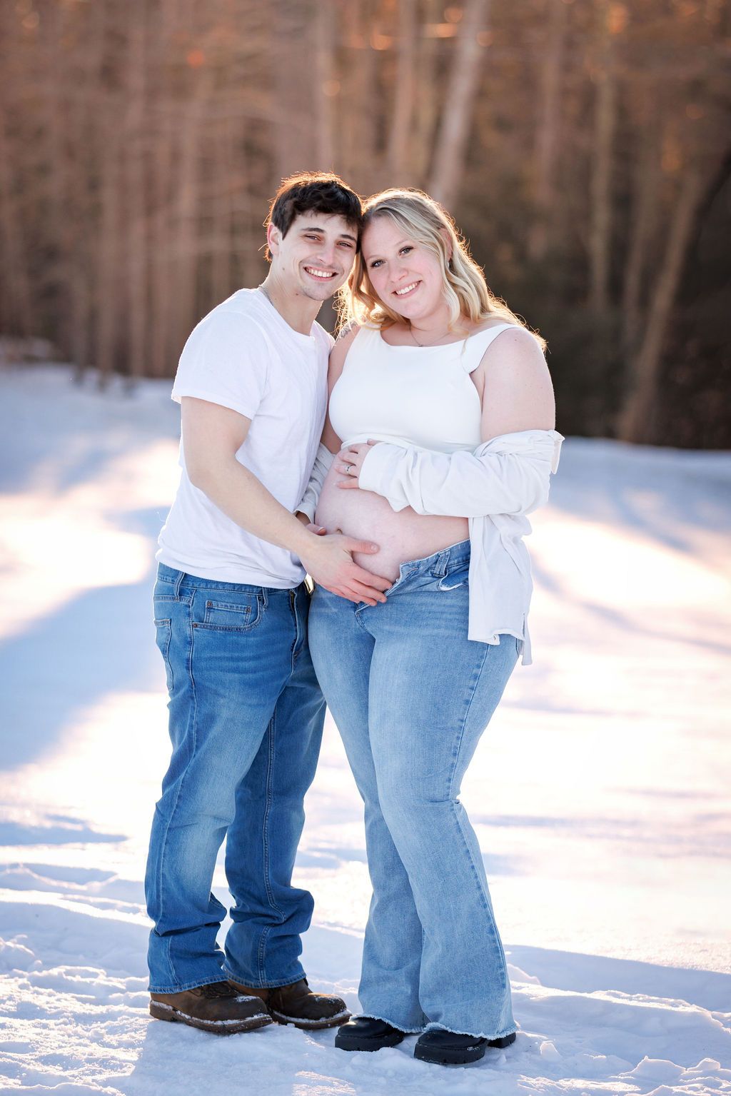 Smiling couple in white tops and jeans posing together outdoors in a snowy winter setting.