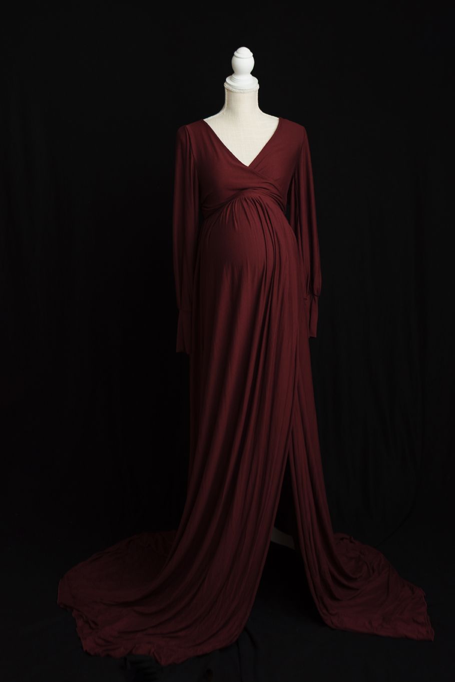 A burgundy maternity dress with long flowing sleeves and v-neckline displayed on a mannequin against black background.