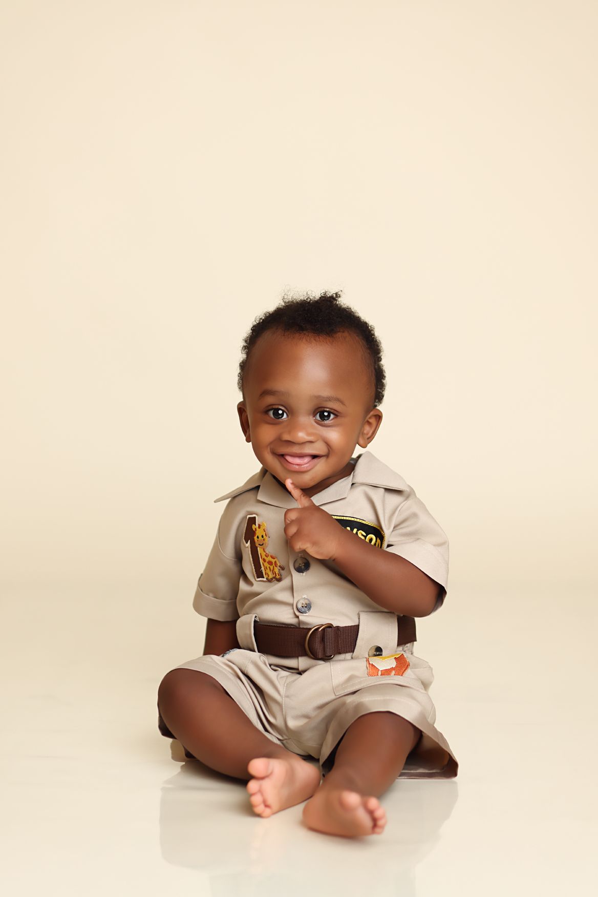 Adorable baby in beige overalls sits and plays in a series of connected portrait photos.