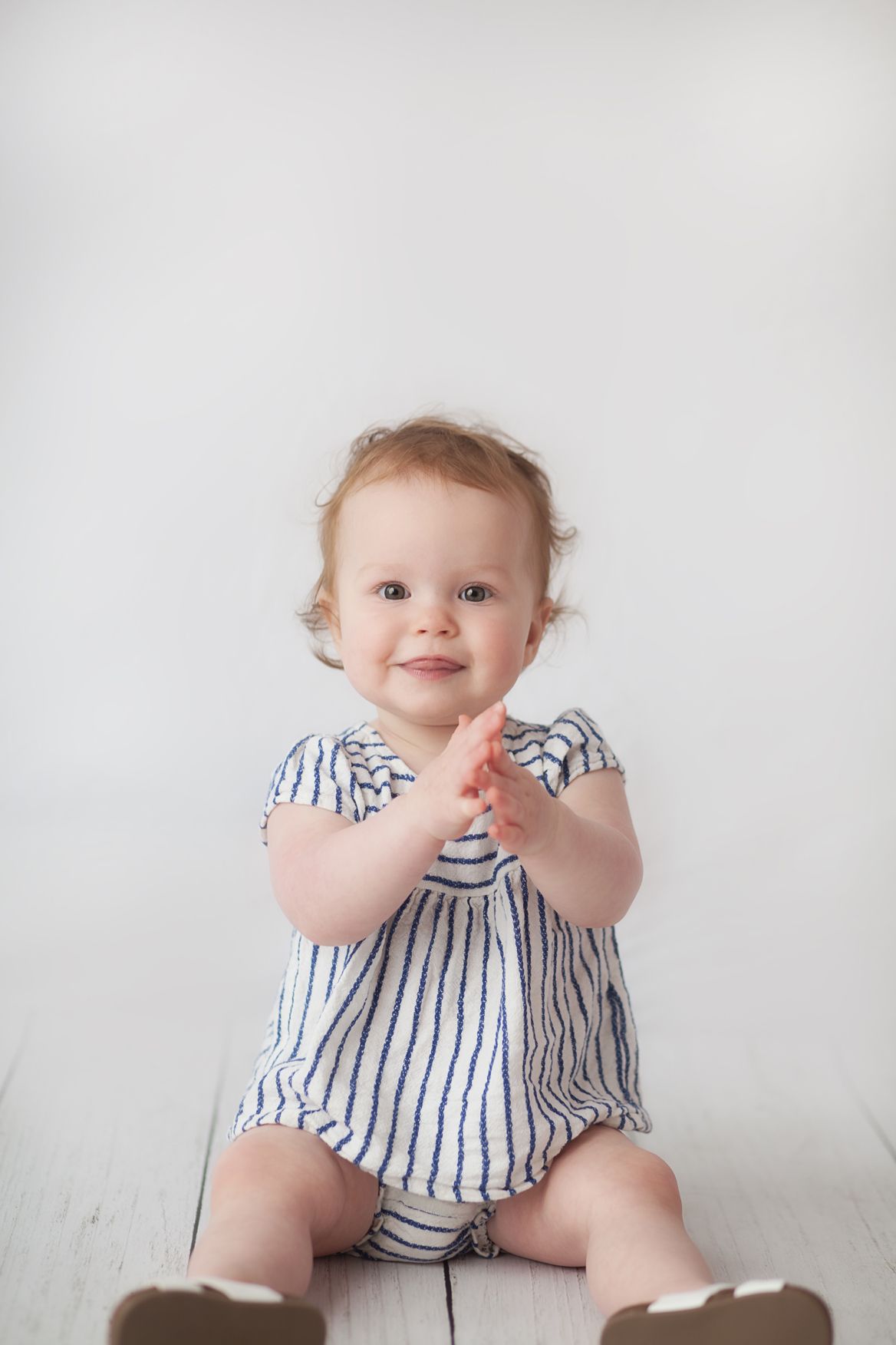 A baby wearing a blue and white striped dress sits on a white background in a progression of four poses.