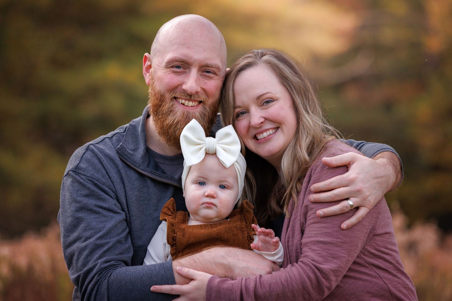 A family poses together in a fall setting with warm autumn colors and foliage in the background.