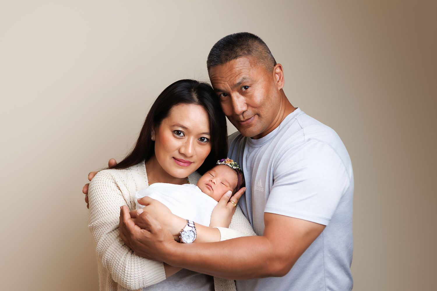 Happy couple holding their sleeping newborn baby in a warm studio portrait photo.