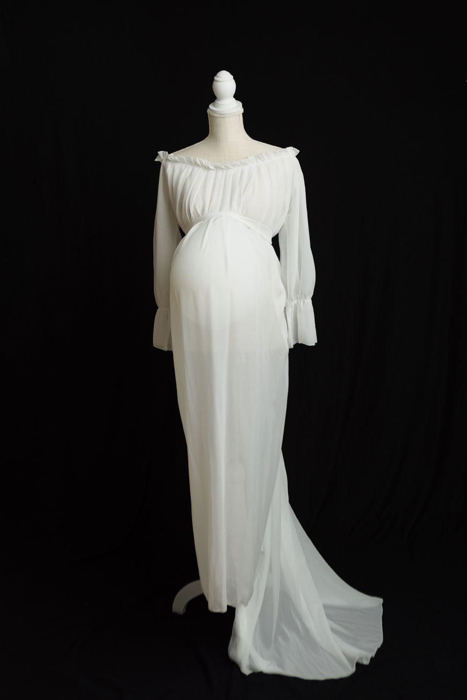 Elegant white flowing chiffon gown with asymmetrical draping and sheer sleeves displayed on a dress form against black background.