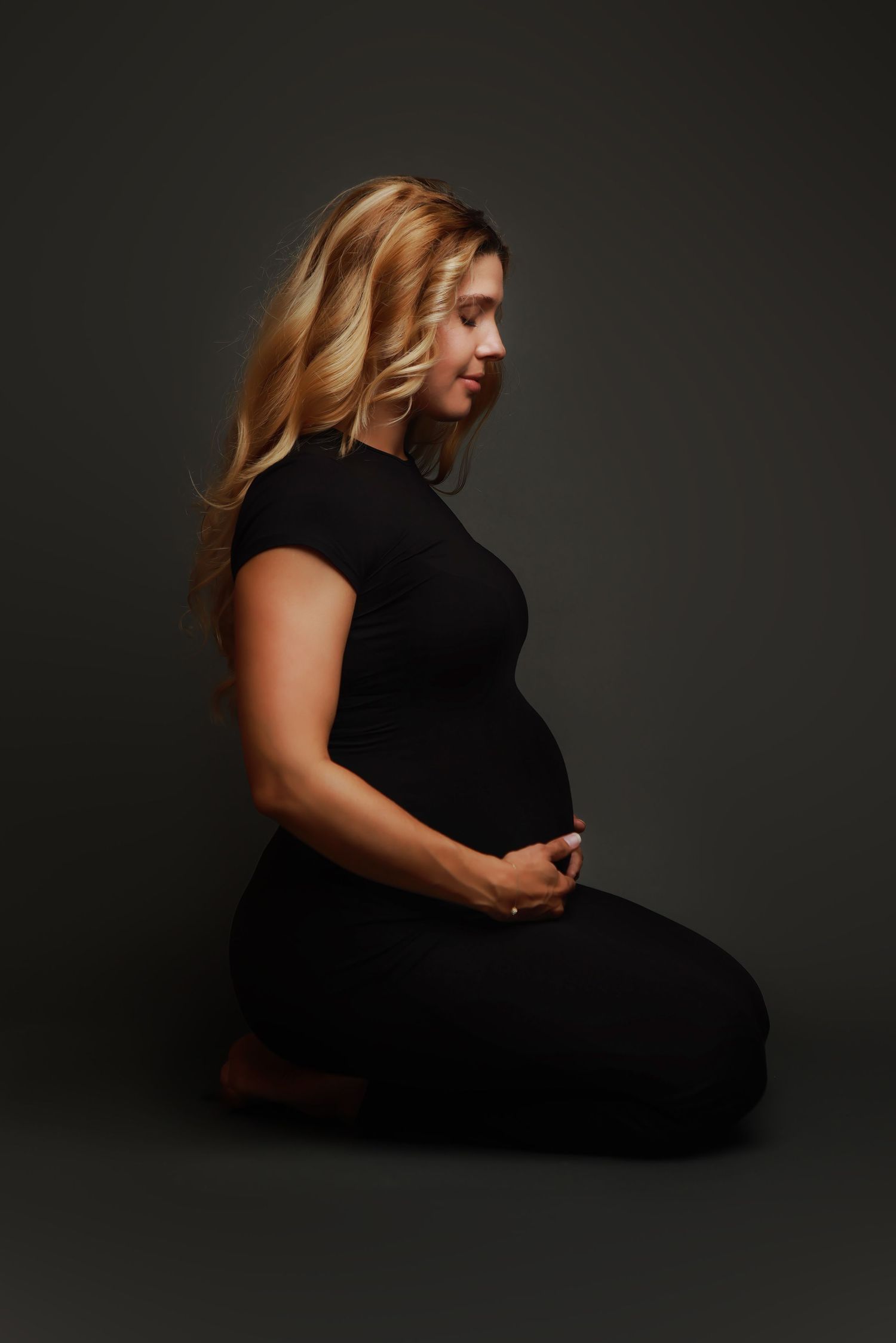 A series of moody black and white Maternity portraits showing a person in a black outfit against a dark background.