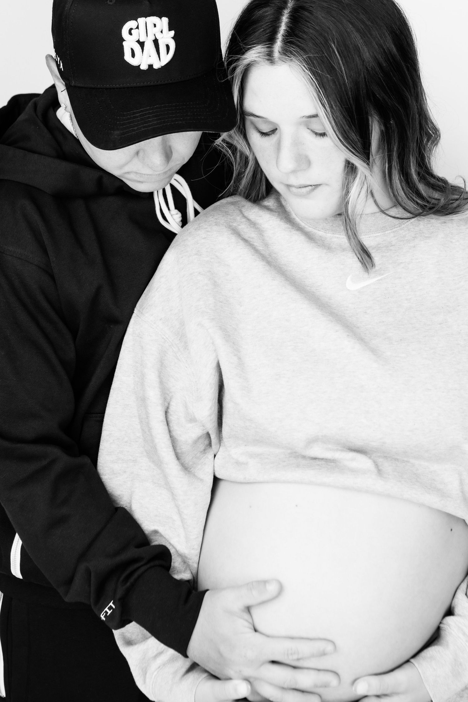 A black and white maternity photo series showing a couple embracing a pregnant belly in matching casual attire.