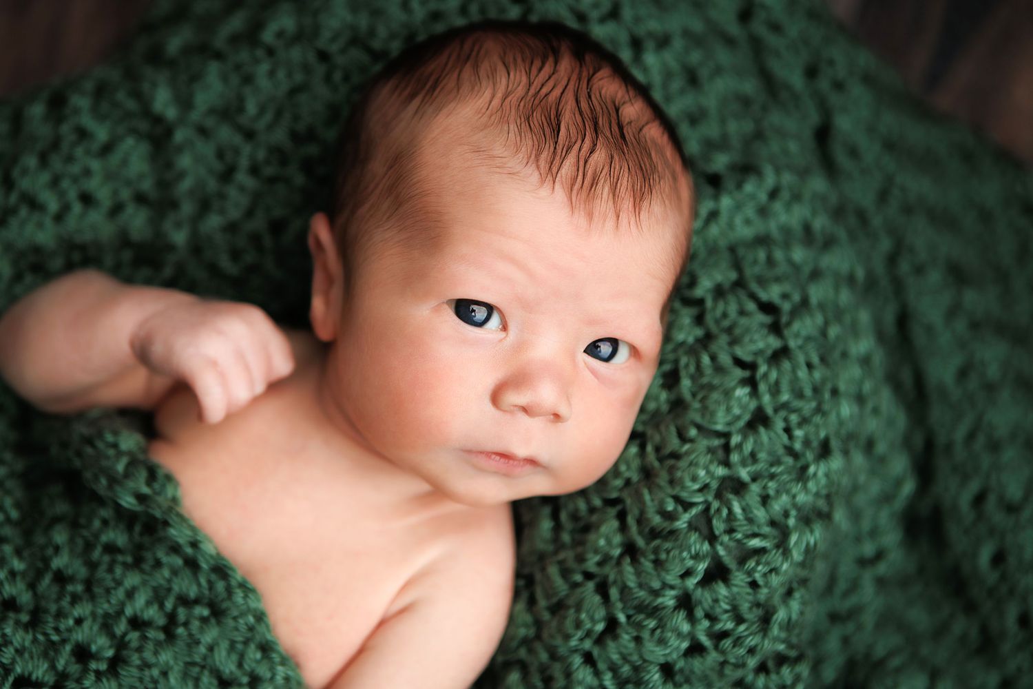 Baby lying on green floral fabric while looking to the side with curious expression.