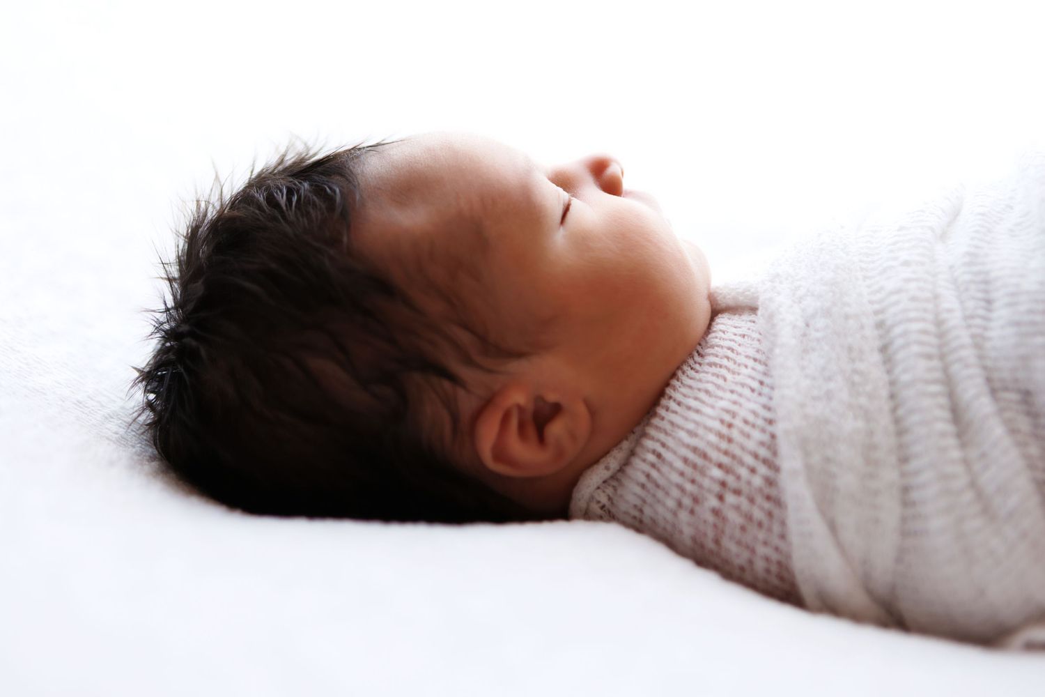 A sleeping infant lies on a white blanket while wearing a cozy knit sweater.
