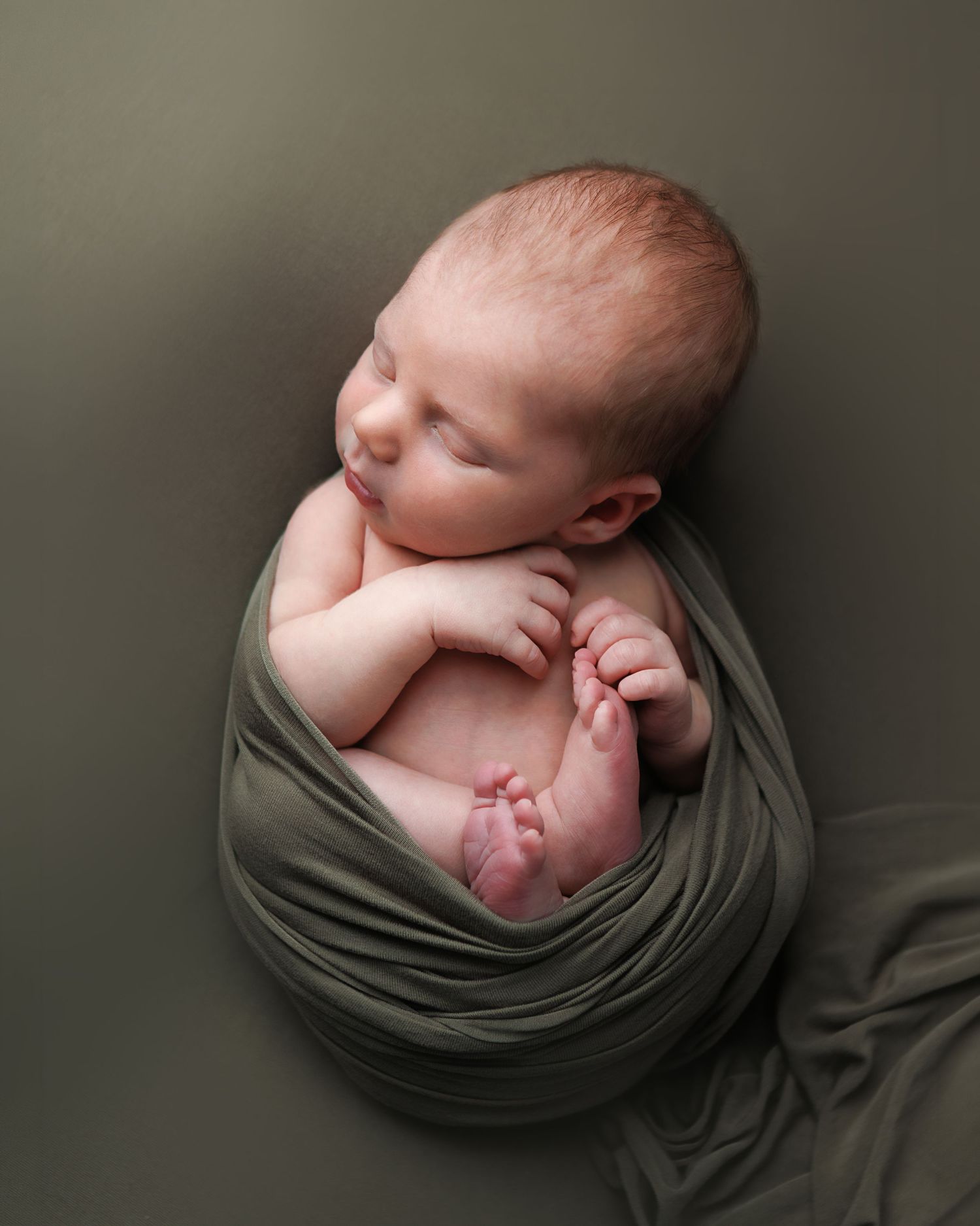 Newborn baby wrapped in olive green during a baby-led newborn photography session in Salem New Hampshire