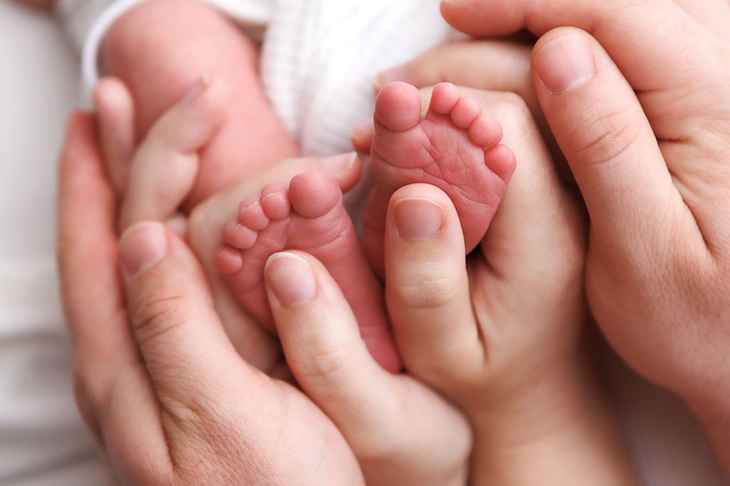 Adult hands gently cradling tiny newborn baby feet, symbolizing love and new parenthood.