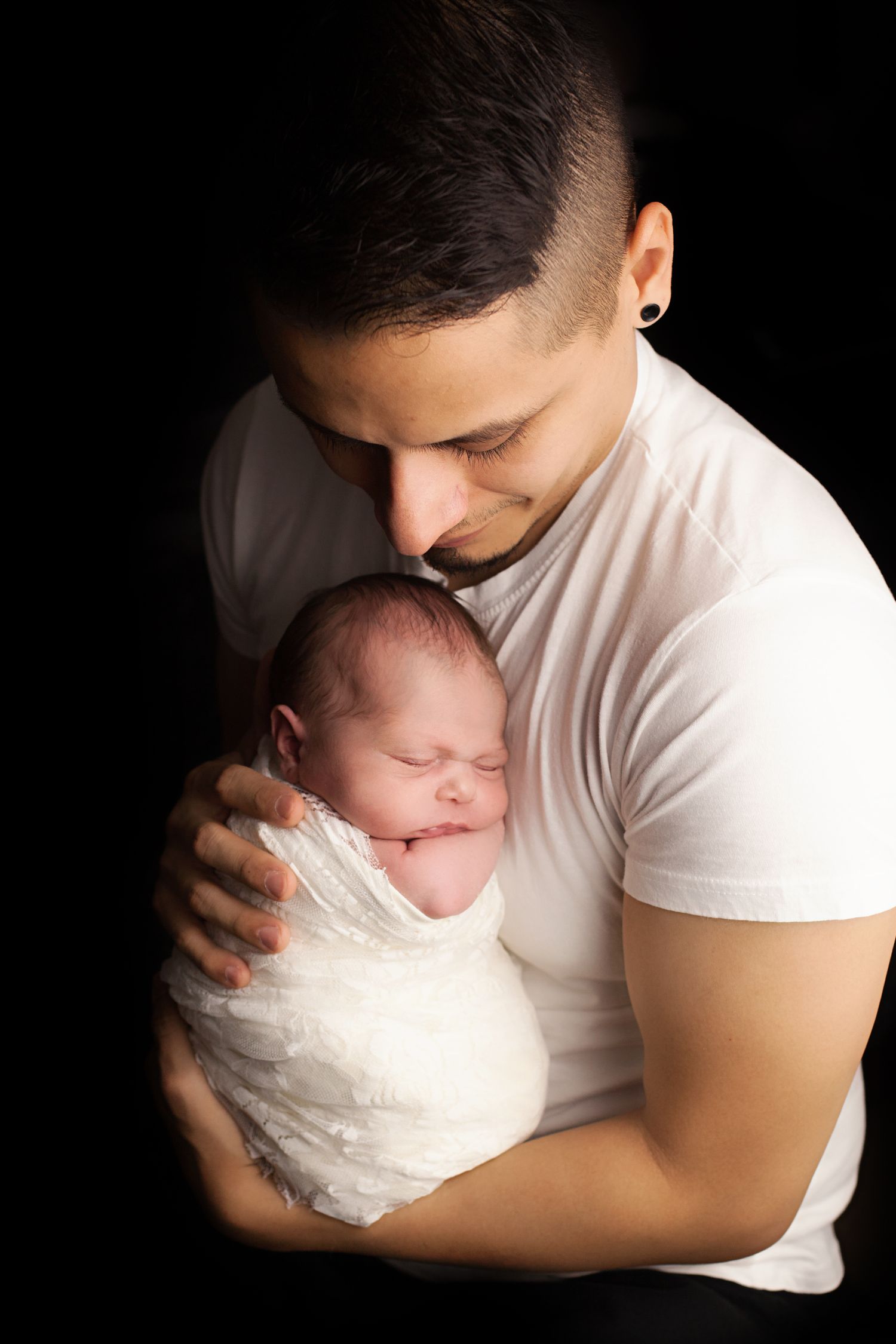 A tender series of black and white photos showing a parent cradling a newborn baby wrapped in white cloth. In-home Hudson NH Newborn Session