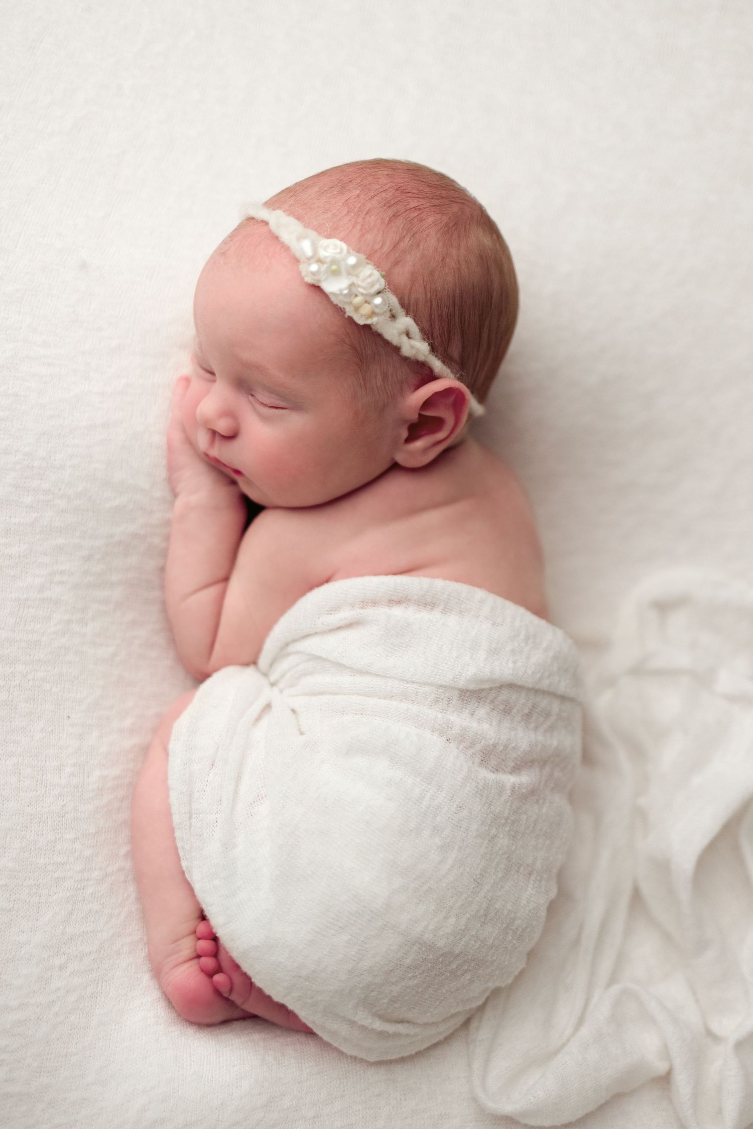 A sleeping newborn baby wrapped in white swaddling cloth lies peacefully on a light background.