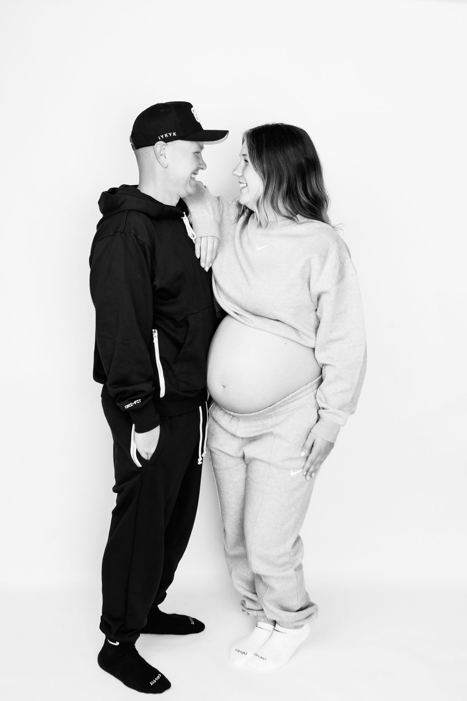 Two figures in contrasting black and white outfits pose together in a minimalist studio setting.
