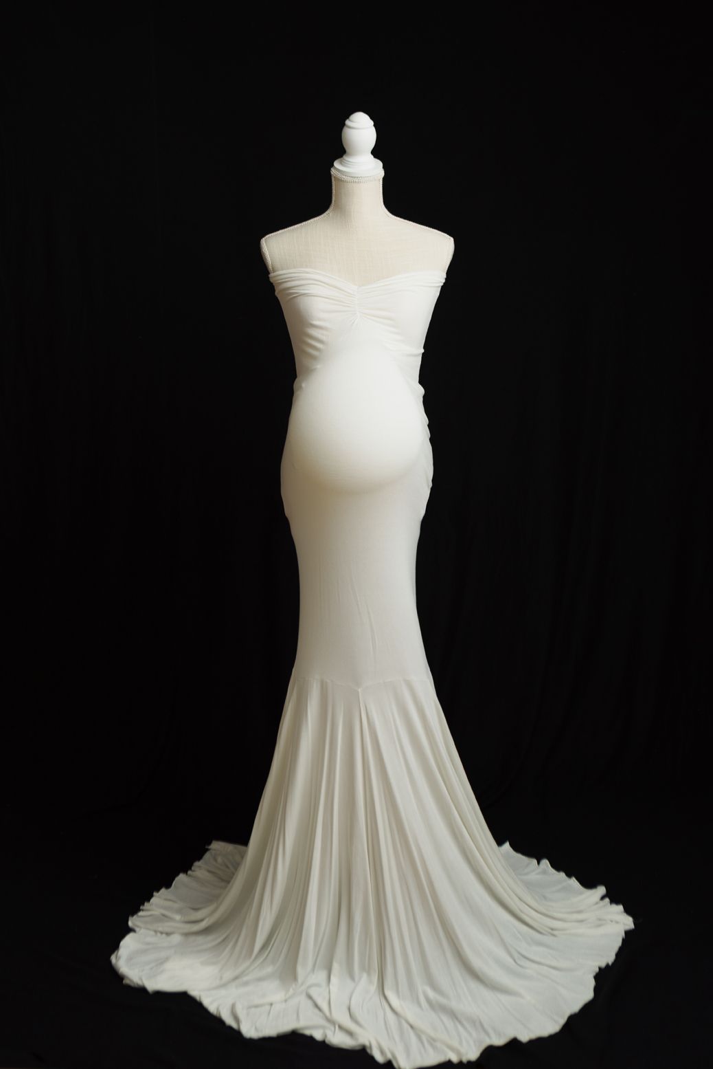 White sleeveless dress form with flowing pleated skirt displayed against black background.