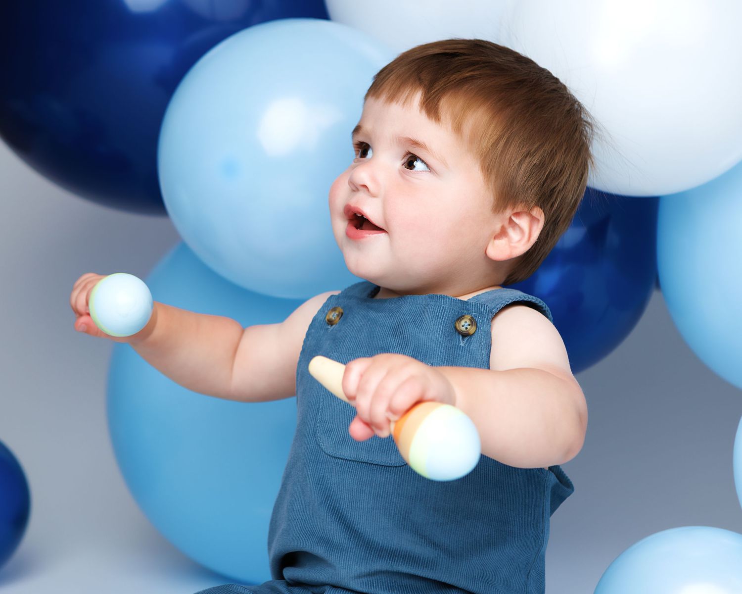 Baby boy in a blue romper playing with wooden toys during his Southern New Hampshire first birthday session