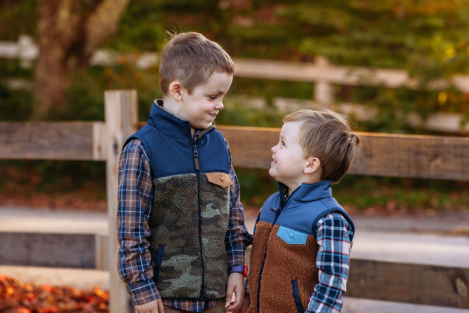 Two children in plaid shirts and jeans playing together outdoors on a wooden structure during autumn.