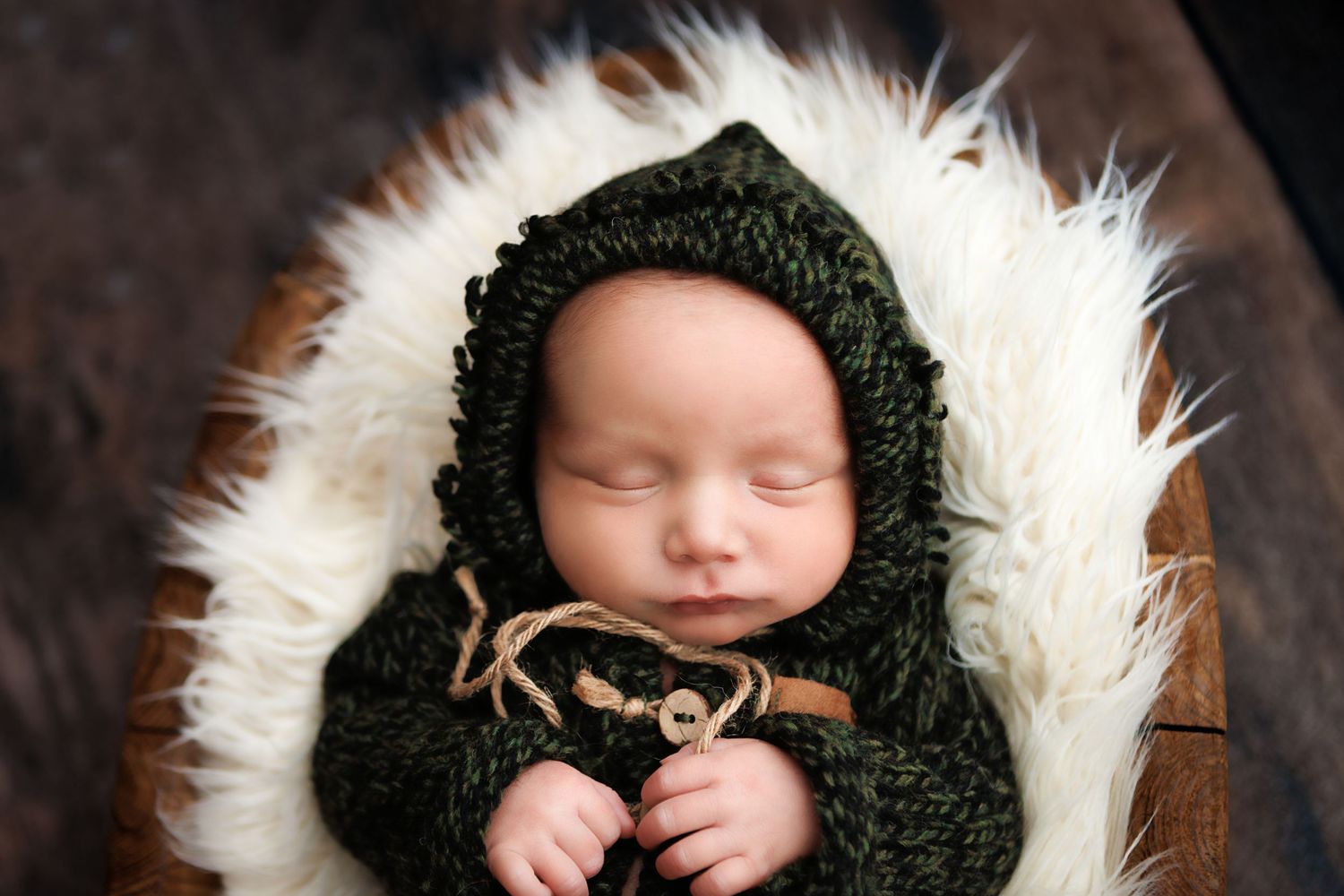 Newborn baby sleeping peacefully in a cozy dark knit wrap against a brown fur backdrop.