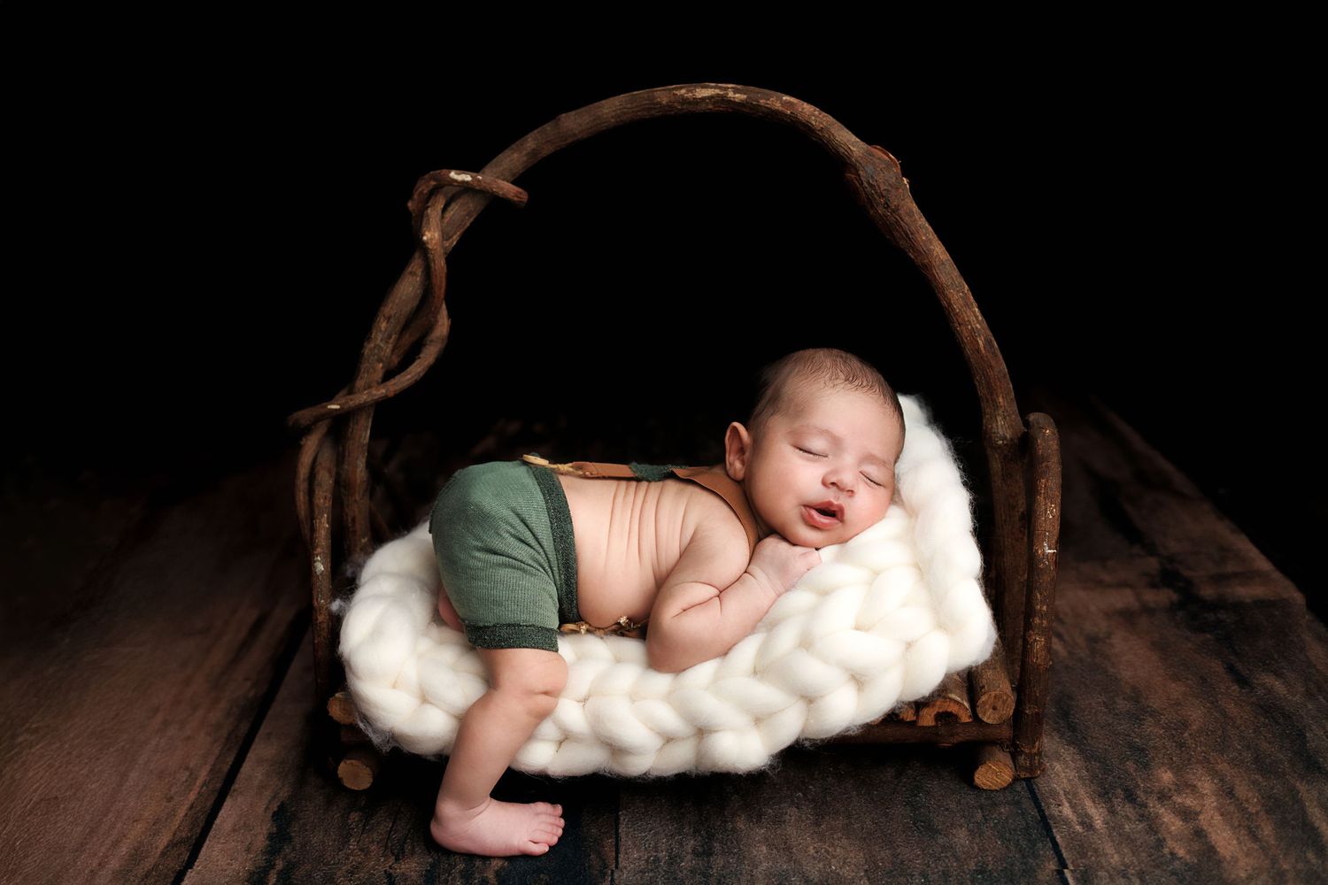 A newborn baby sleeps peacefully on dark wooden floor while wrapped in soft white blankets. Salem NH Newborn Session