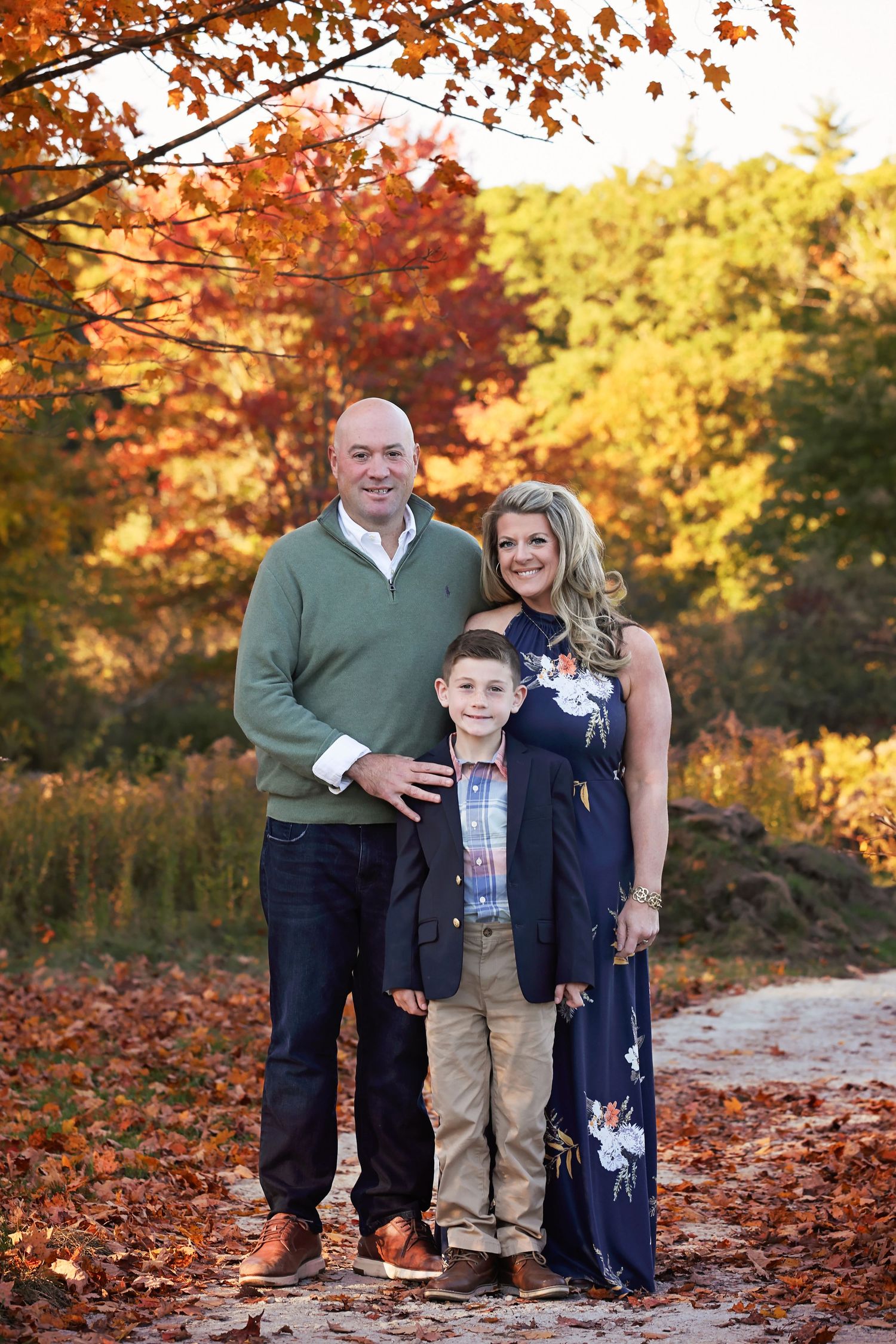 A family poses together on a path surrounded by vibrant fall foliage in orange and yellow hues.