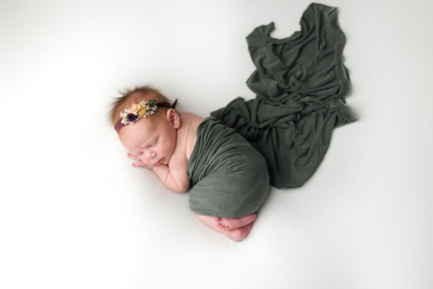 Artistic collage of newborn baby photos with flowing dark green fabric against white background.