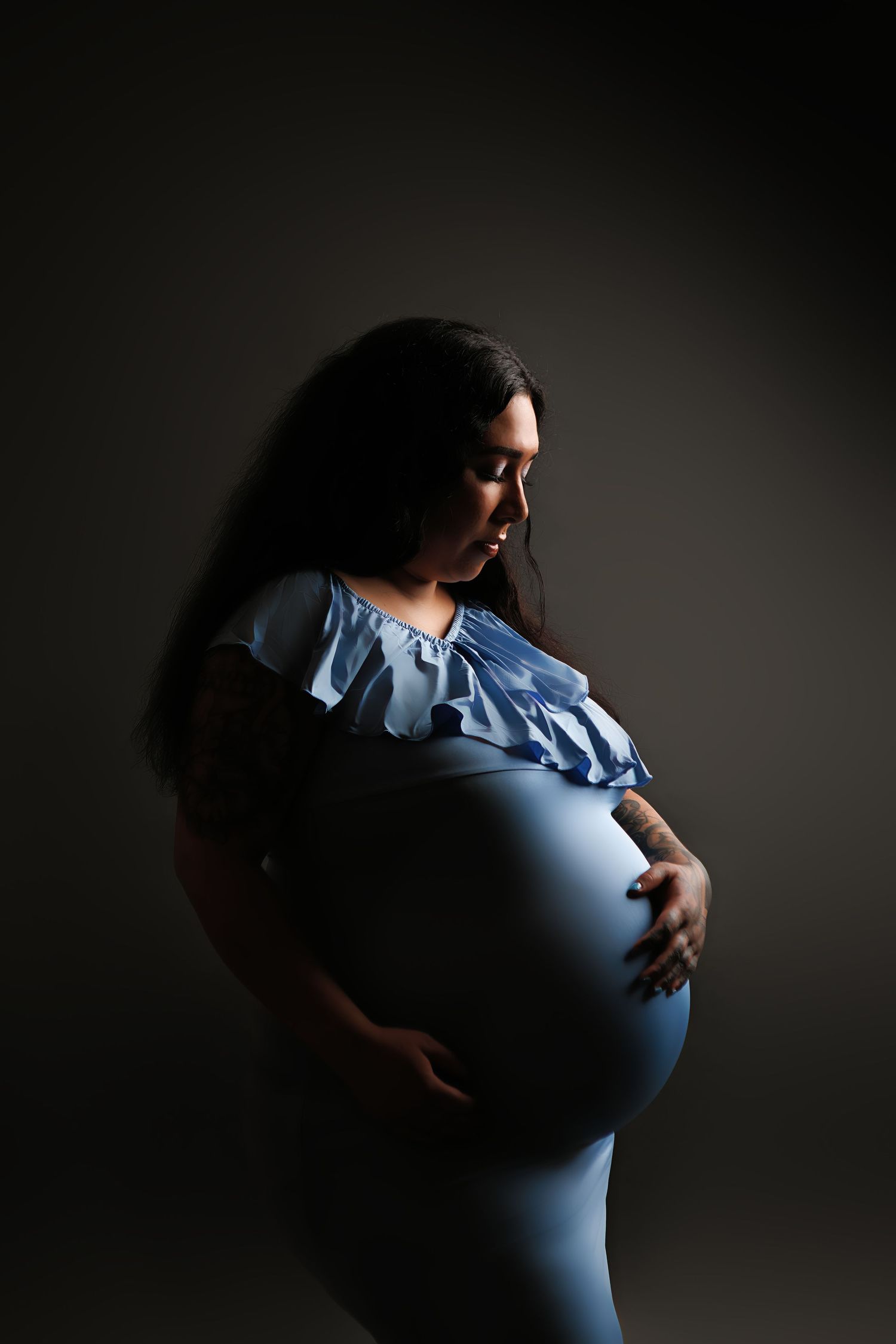 A series of dramatic maternity photos showing a pregnant silhouette against a dark background wearing a blue ruffled top.