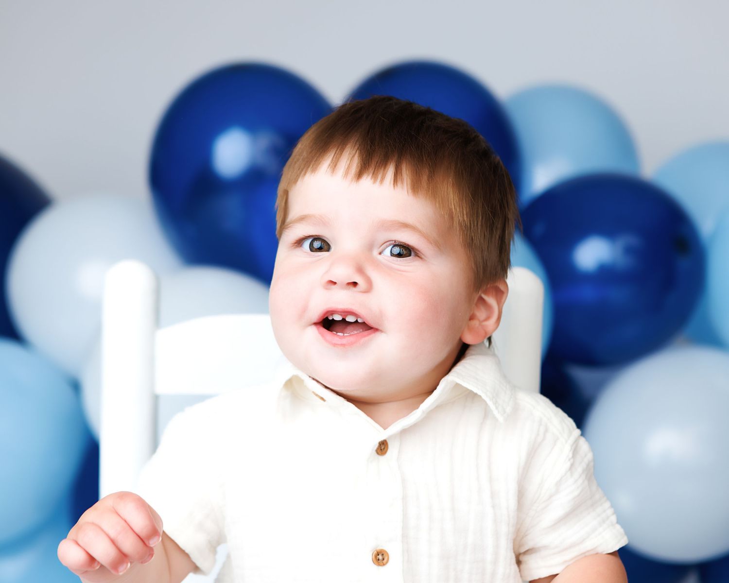 Smiling baby boy photographed with a blue balloon backdrop for first birthday portraits in Salem New Hampshire