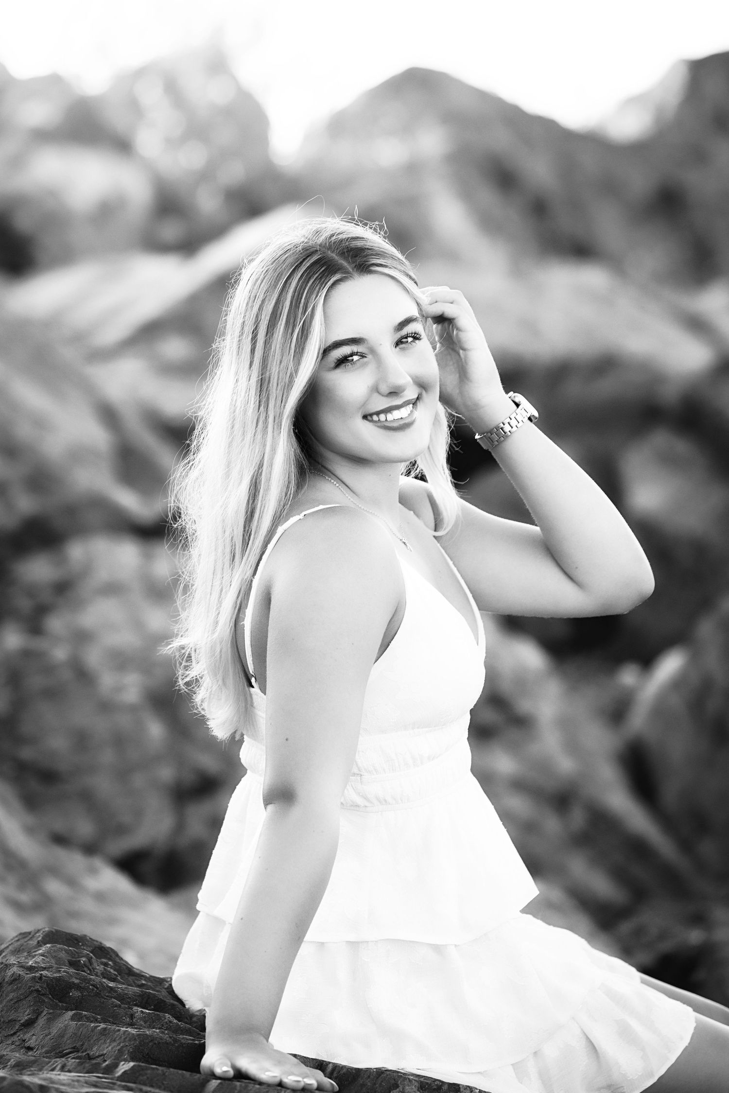 Windham NH Senior in a white dress poses joyfully on rocks in a black and white outdoor photoshoot.