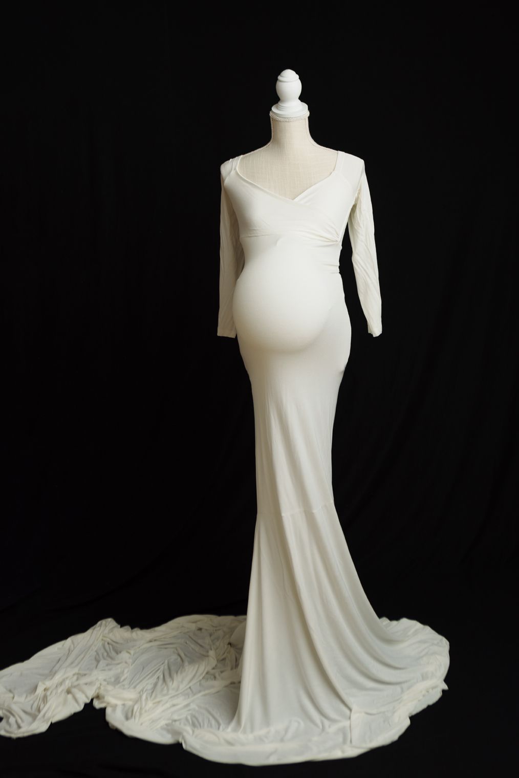 Elegant white wedding dress with sleek silhouette and dramatic train displayed on mannequin against black background.