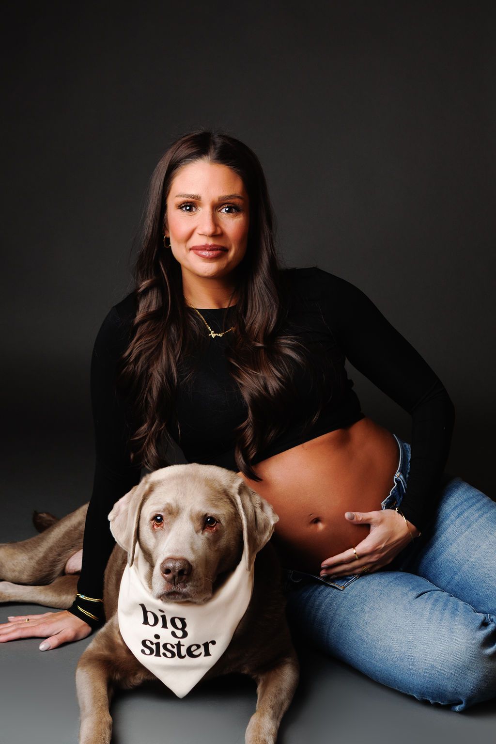 Pregnant woman in black crop top with Weimaraner dog wearing big sister bandana.