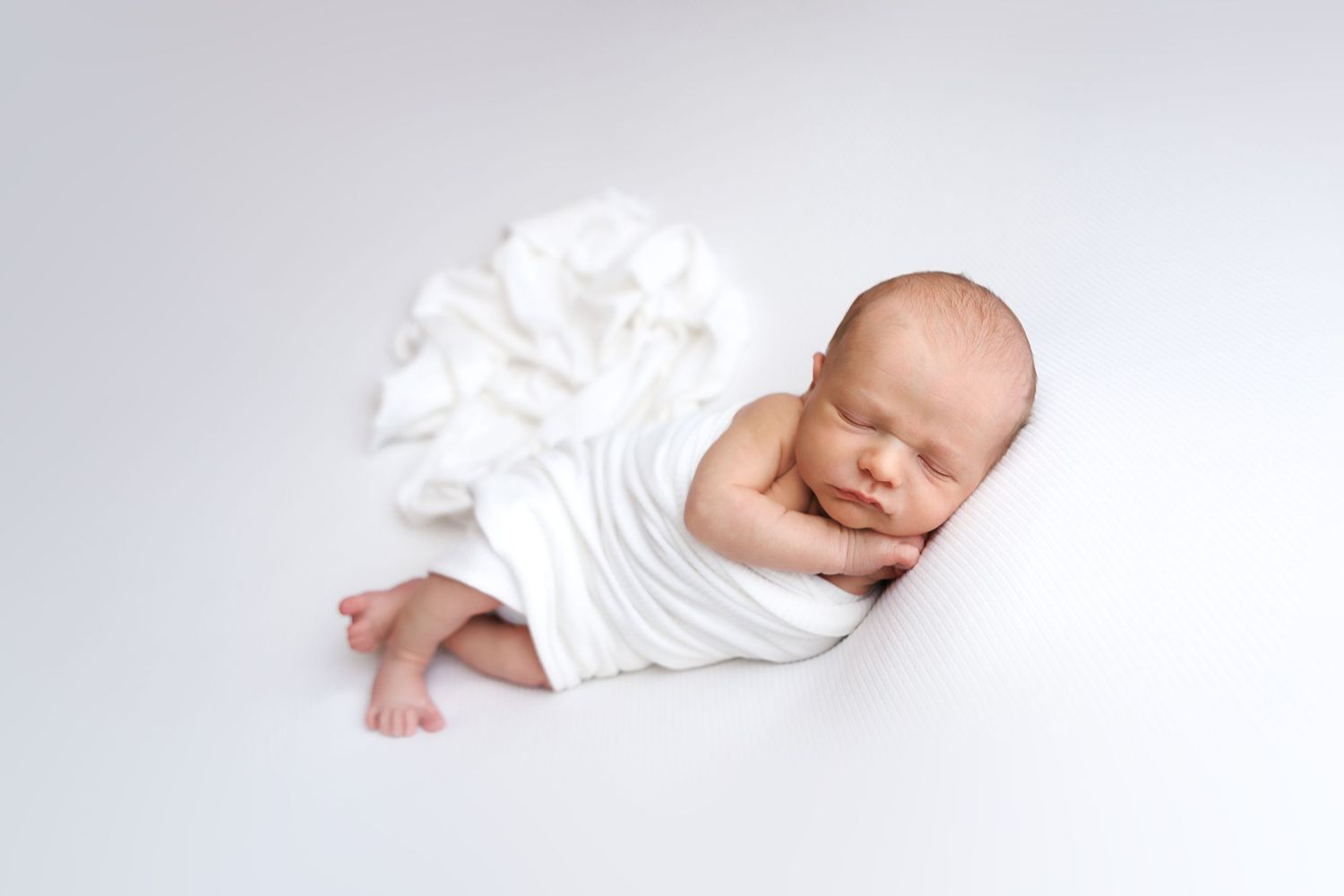 Peaceful newborn baby sleeping wrapped in white cloth on a white background in a professional photo.