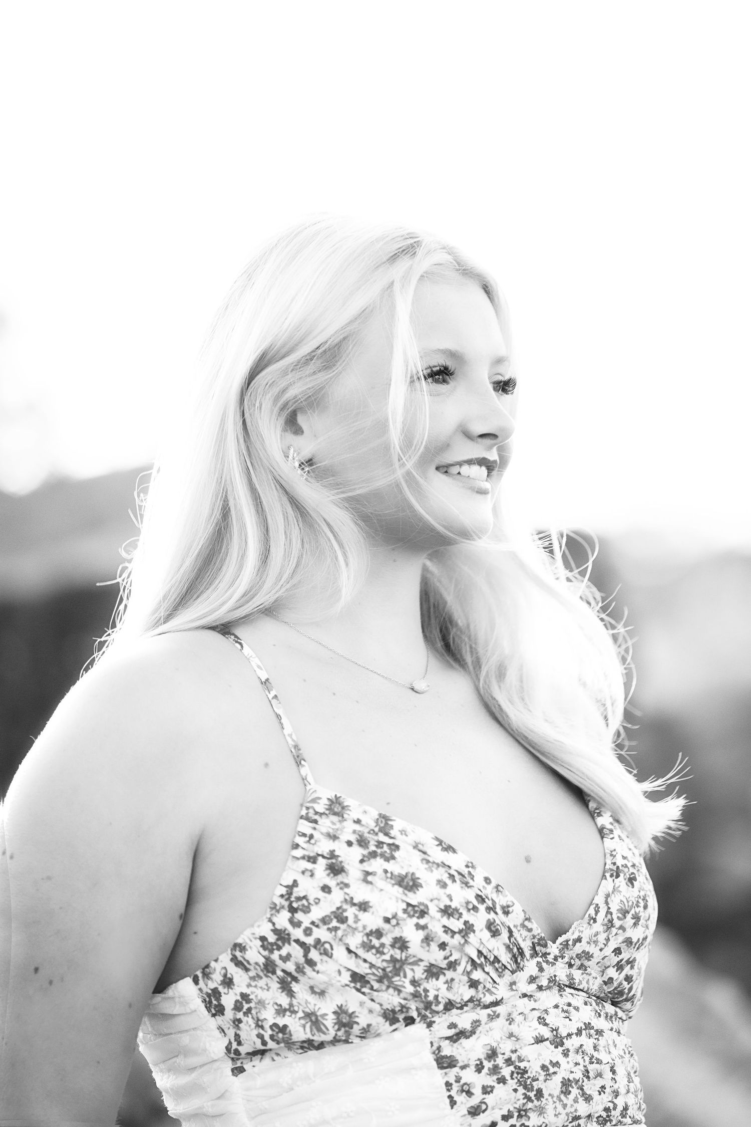 Black and white portrait of smiling blonde woman in floral dress in bright sunlight.