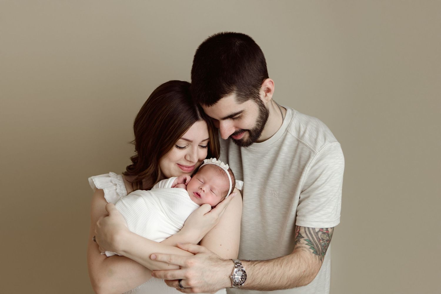 A newborn baby sleeps peacefully while being held against a neutral beige background.