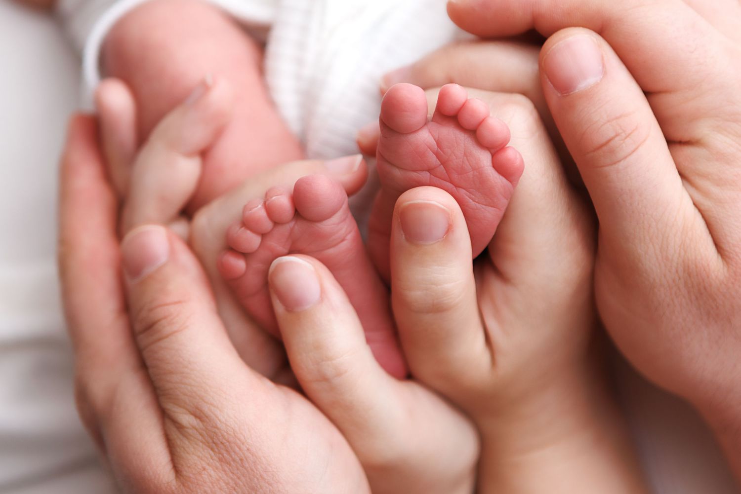 Adult hands gently cradling tiny newborn baby feet, symbolizing love and parental care.