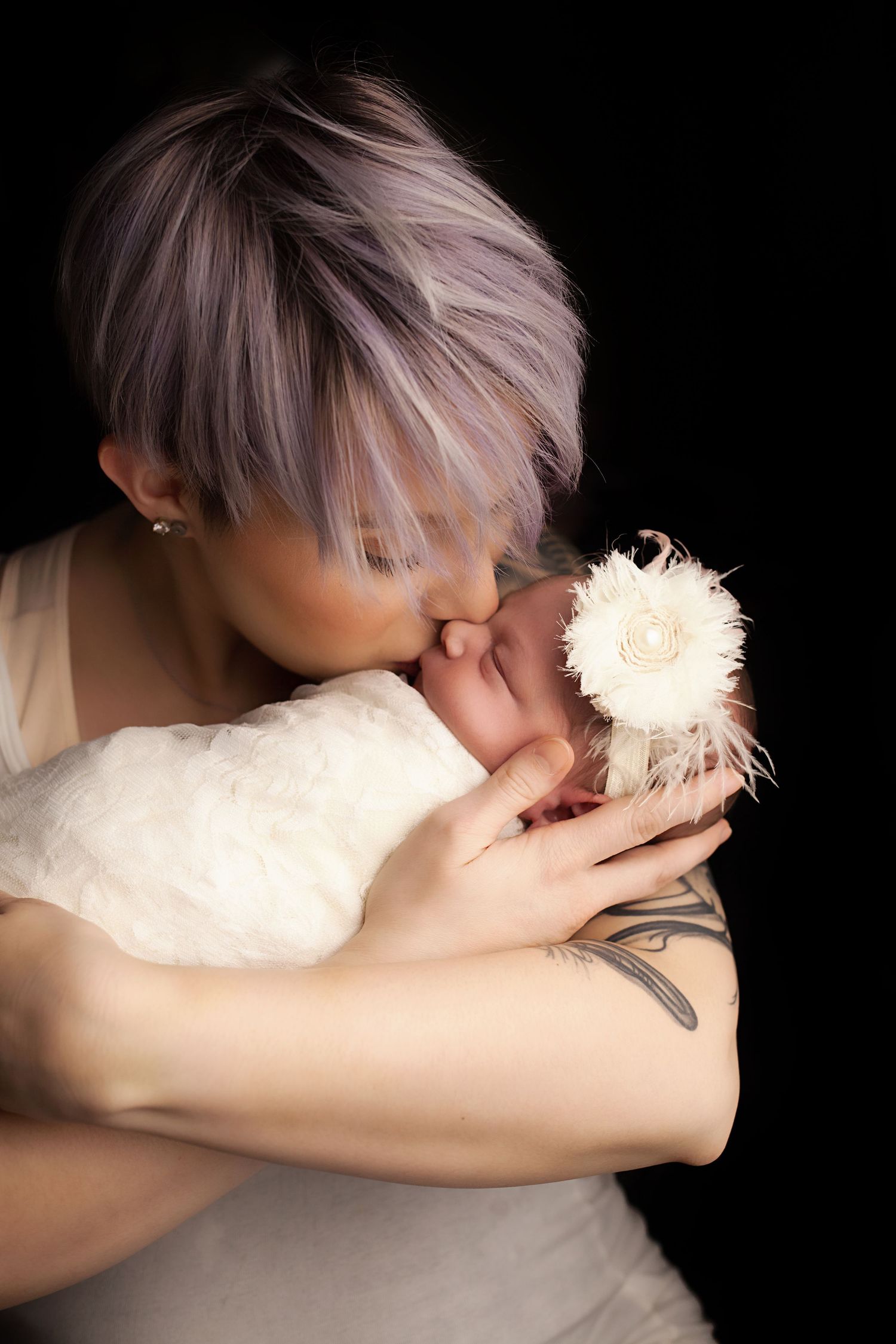 Mother with pastel hair gently kissing a white fluffy cat against dark background in artistic portrait series.