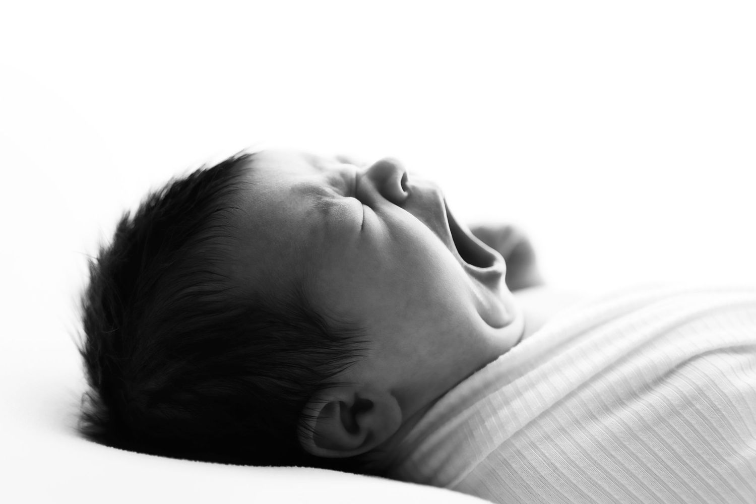 Black and white portrait of a sleeping baby lying on white bedding.