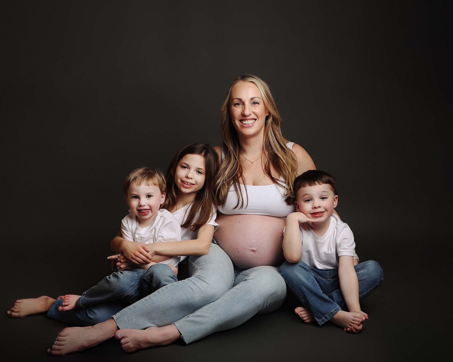 Maternity photo series showing family members lying together on black background in casual attire.
