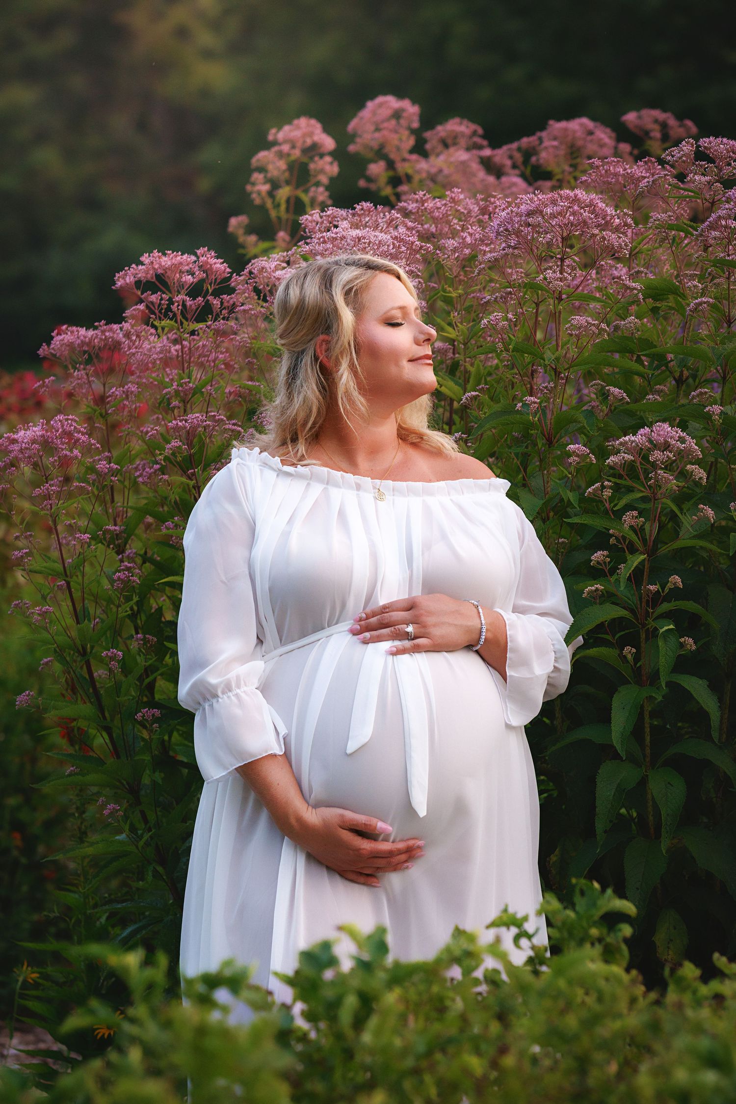 A maternity photoshoot in a garden with pink Joe Pye weed flowers creating a romantic natural backdrop.