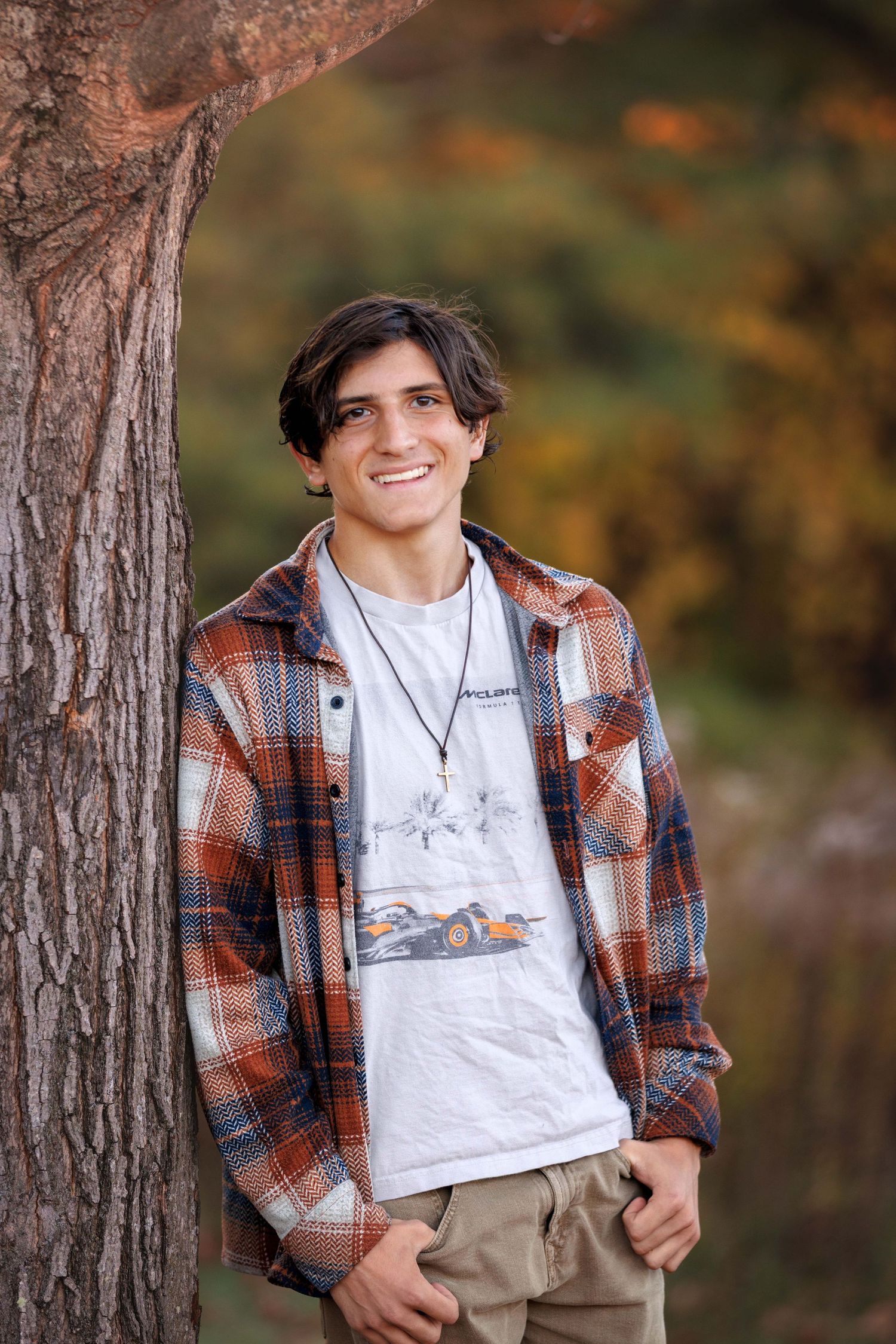 Casual outdoor portrait series showing Senior in a plaid flannel shirt and white t-shirt against autumn trees.